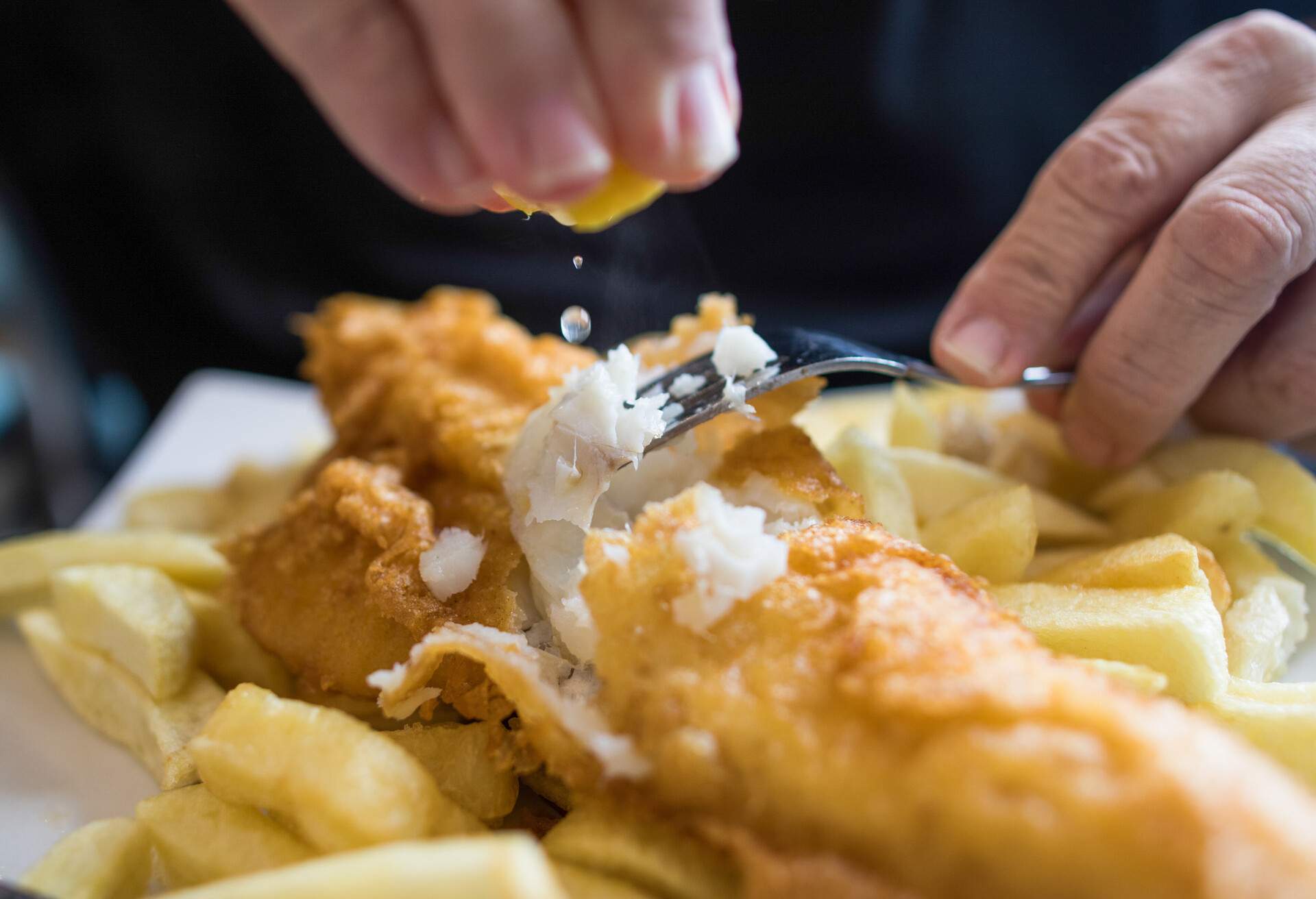A man squeezing fresh lemon juice over his fish and chips.