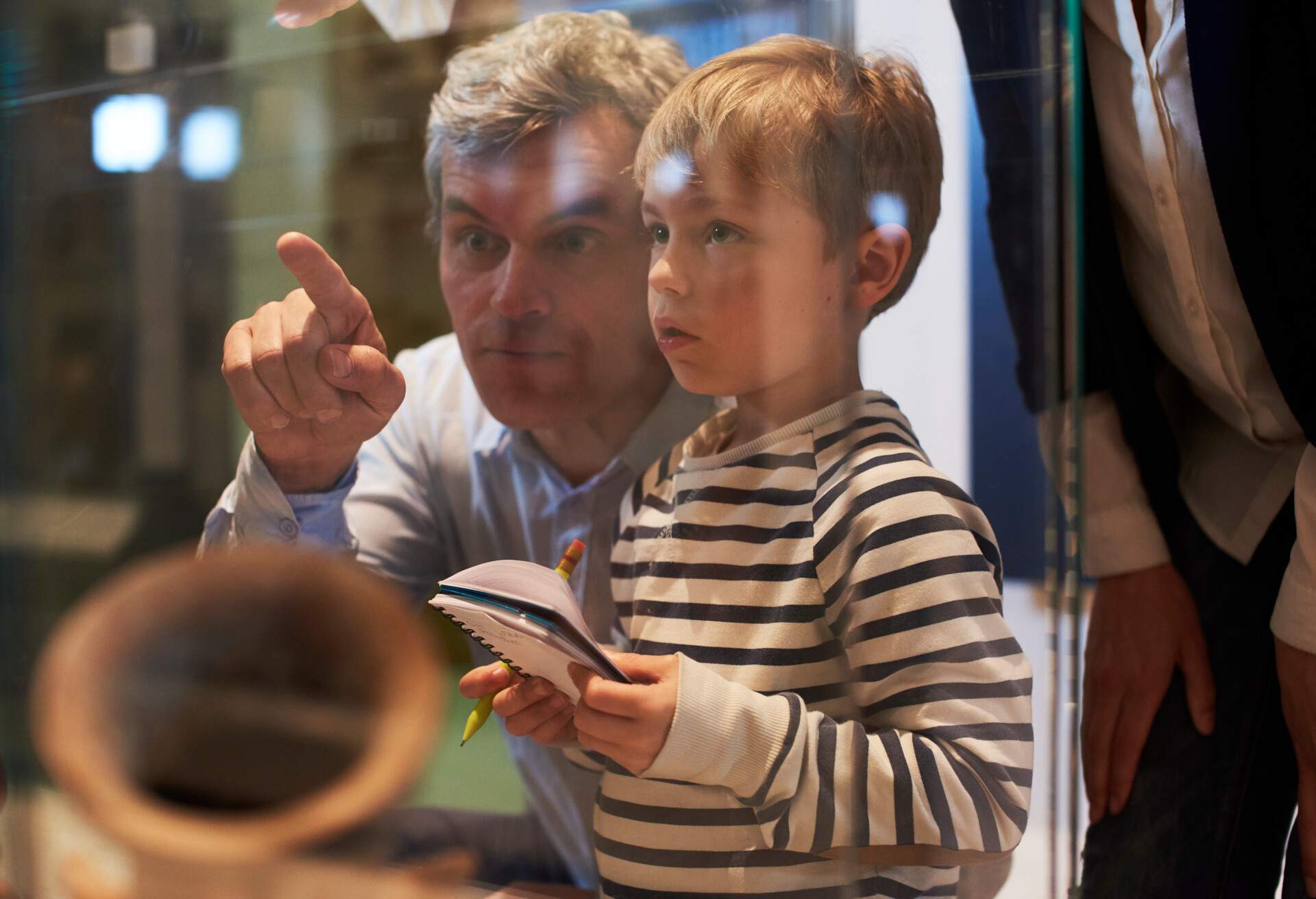 A father pointing at a display in a glass case as the son takes notes.
