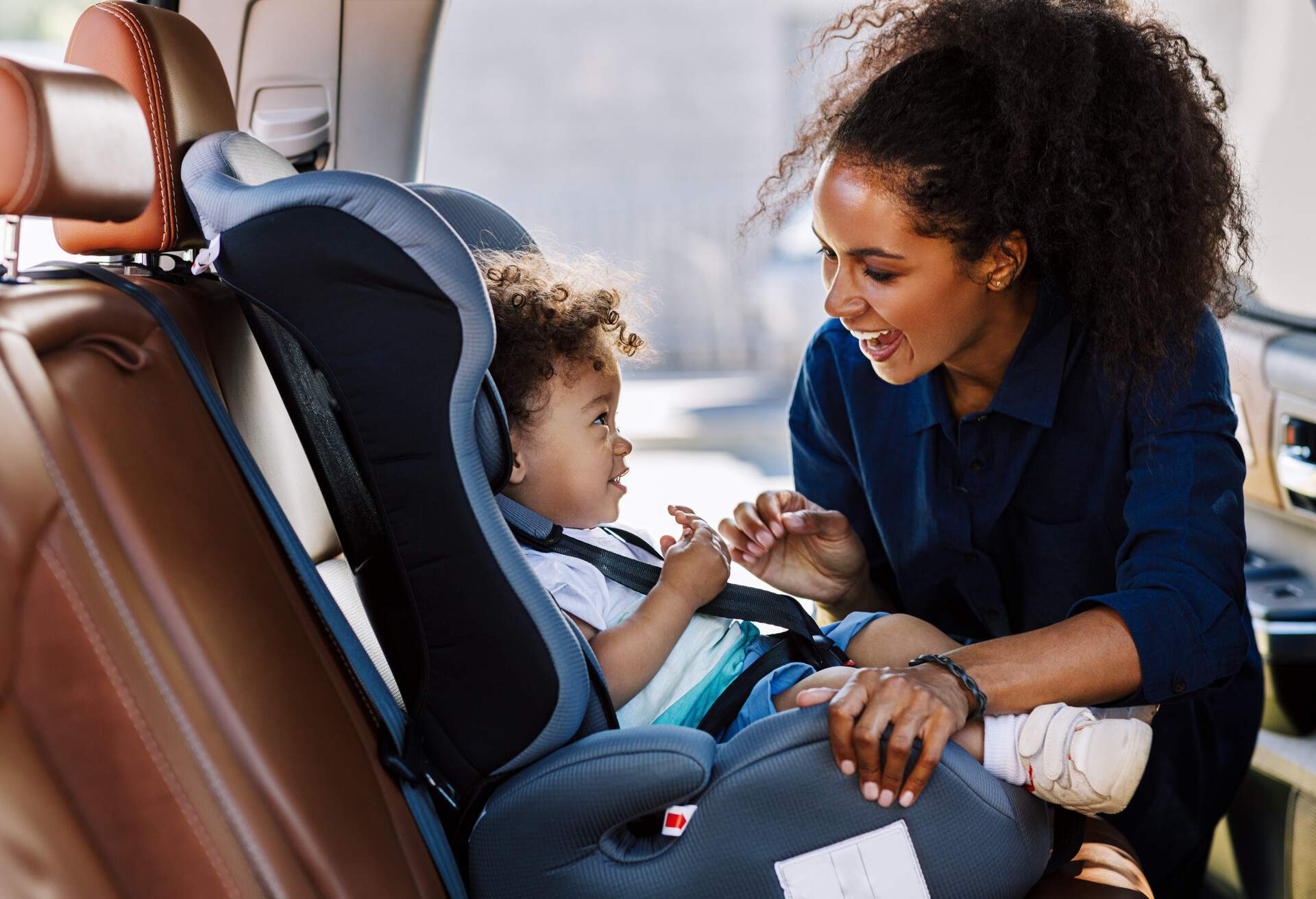 Happy mother looking at her son in a baby seat. Young female preparing kid for a trip.