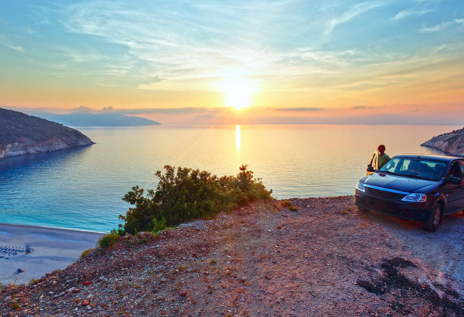 Sea sunset view of Myrtos Beach and woman near car (Greece,  Kefalonia, Ionian Sea).