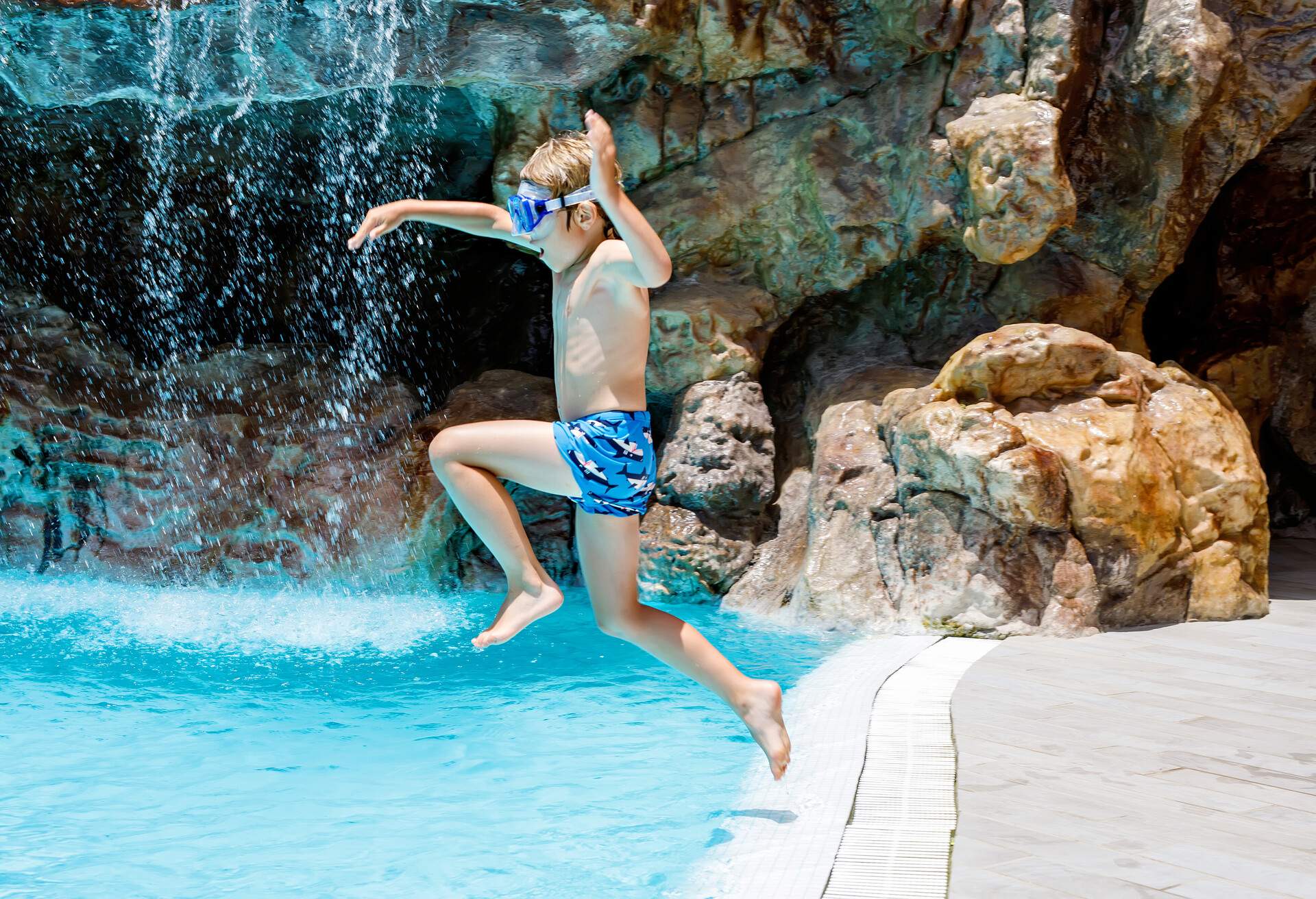 Happy little kid boy jumping in the pool and having fun on family vacations in a hotel resort. Healthy child playing in water.