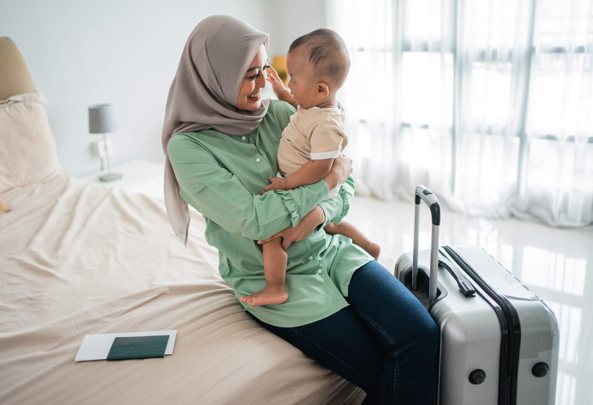 Muslim Asian mothers carry their babies while sitting on the bed before leaving with a suitcase