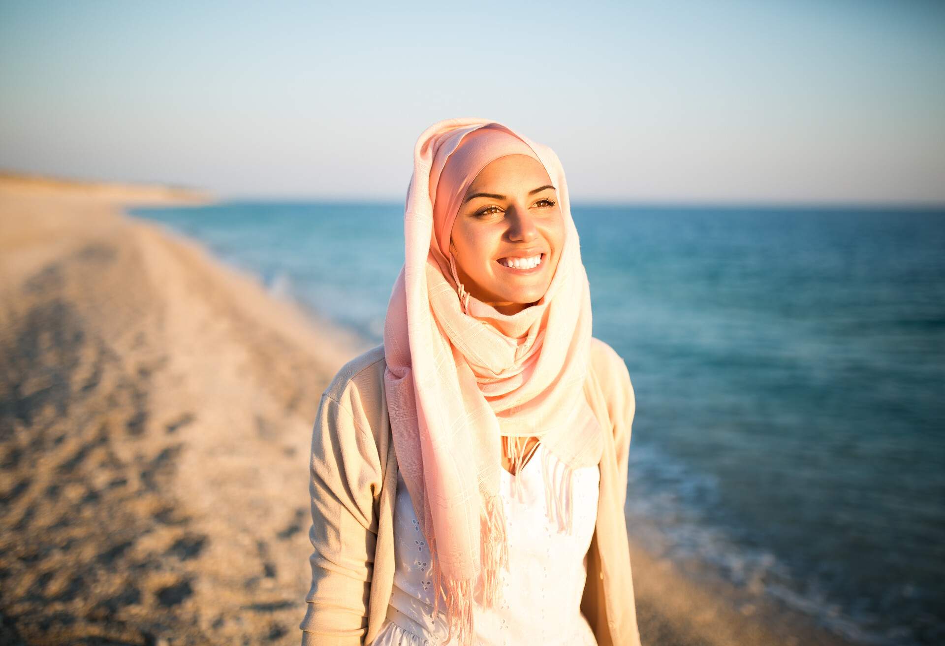 Young beautiful happy muslim woman outdoors portrait.Seaside,beach walk.Beautiful arab saudi woman face posing on the beach with the sea in the background
