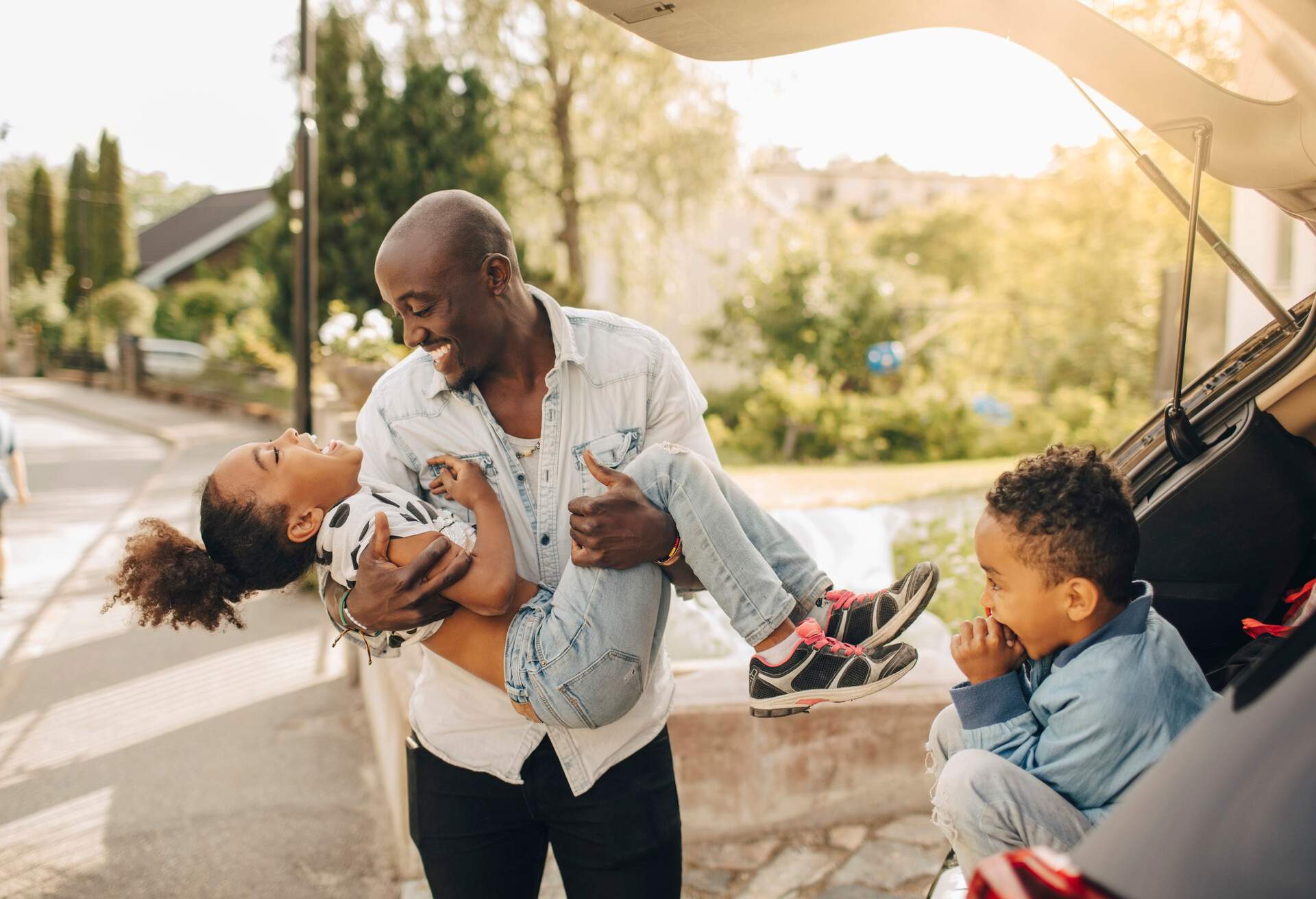 Boy looking at cheerful father carrying daughter by electric car on driveway