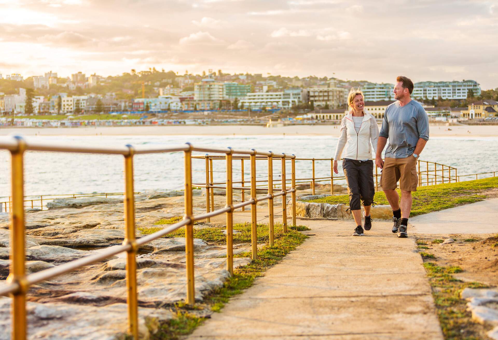 Happy and healthy middle aged active and fit couple walking outdoors by the seaside at Bondi Beach in Sydney, Australia at sunset