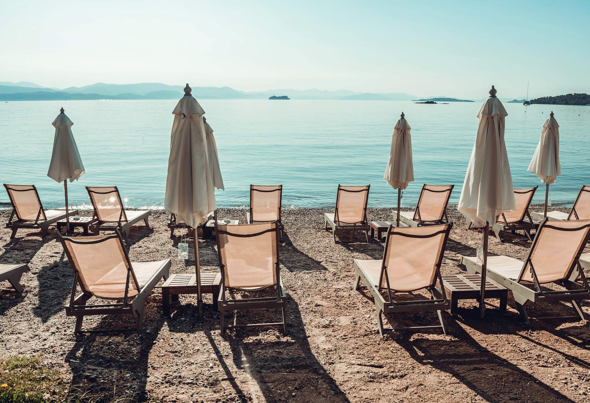 Dassia resort on Corfu, Greece – beach with golden sand, umbrellas and chairs. Summer landscape with parasols, sunbeds, palm trees and blue sky and sea on the horizon.