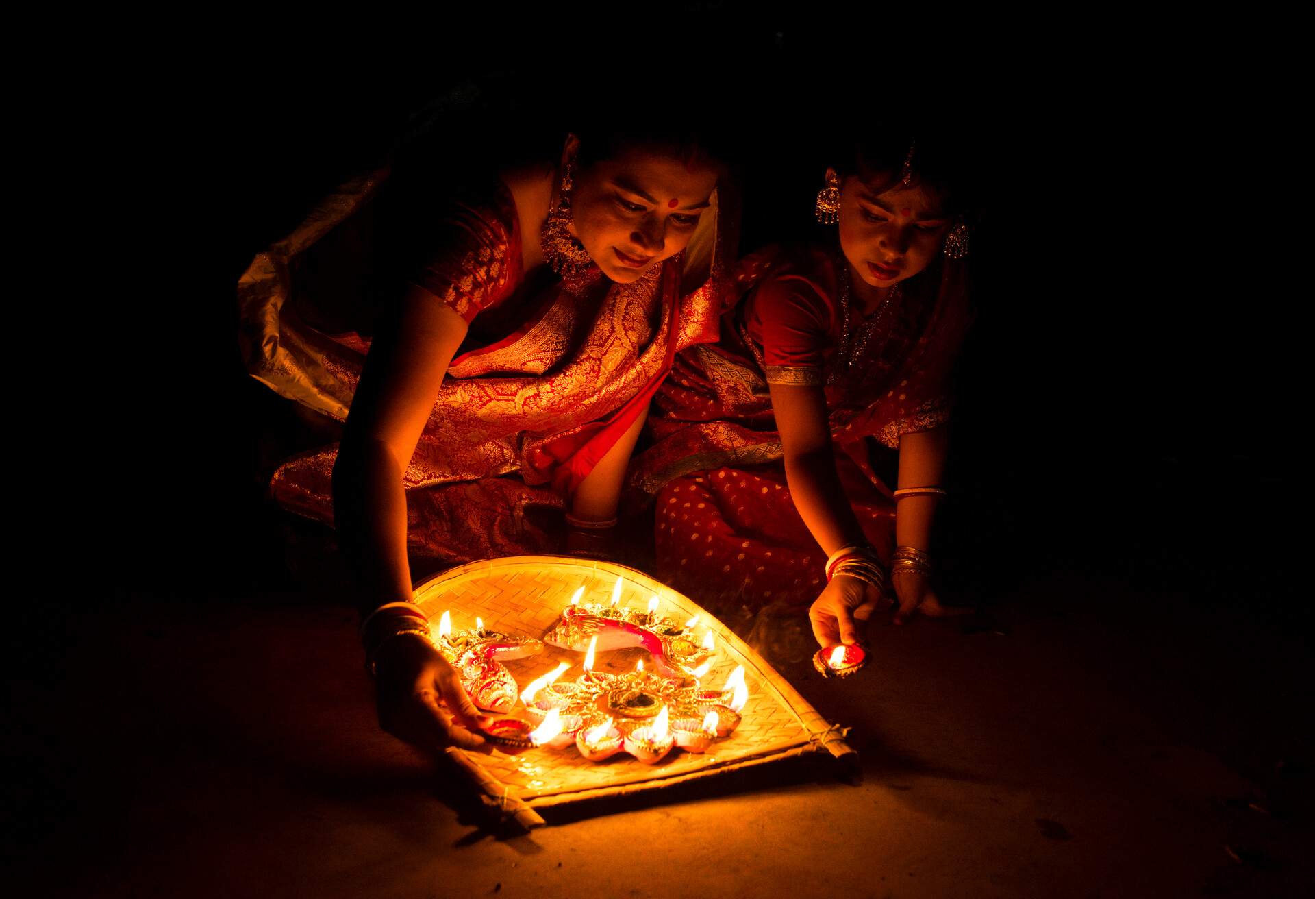 Two Indian ladies lit candles on clay lamps in their homes to celebrate the festival of lights.