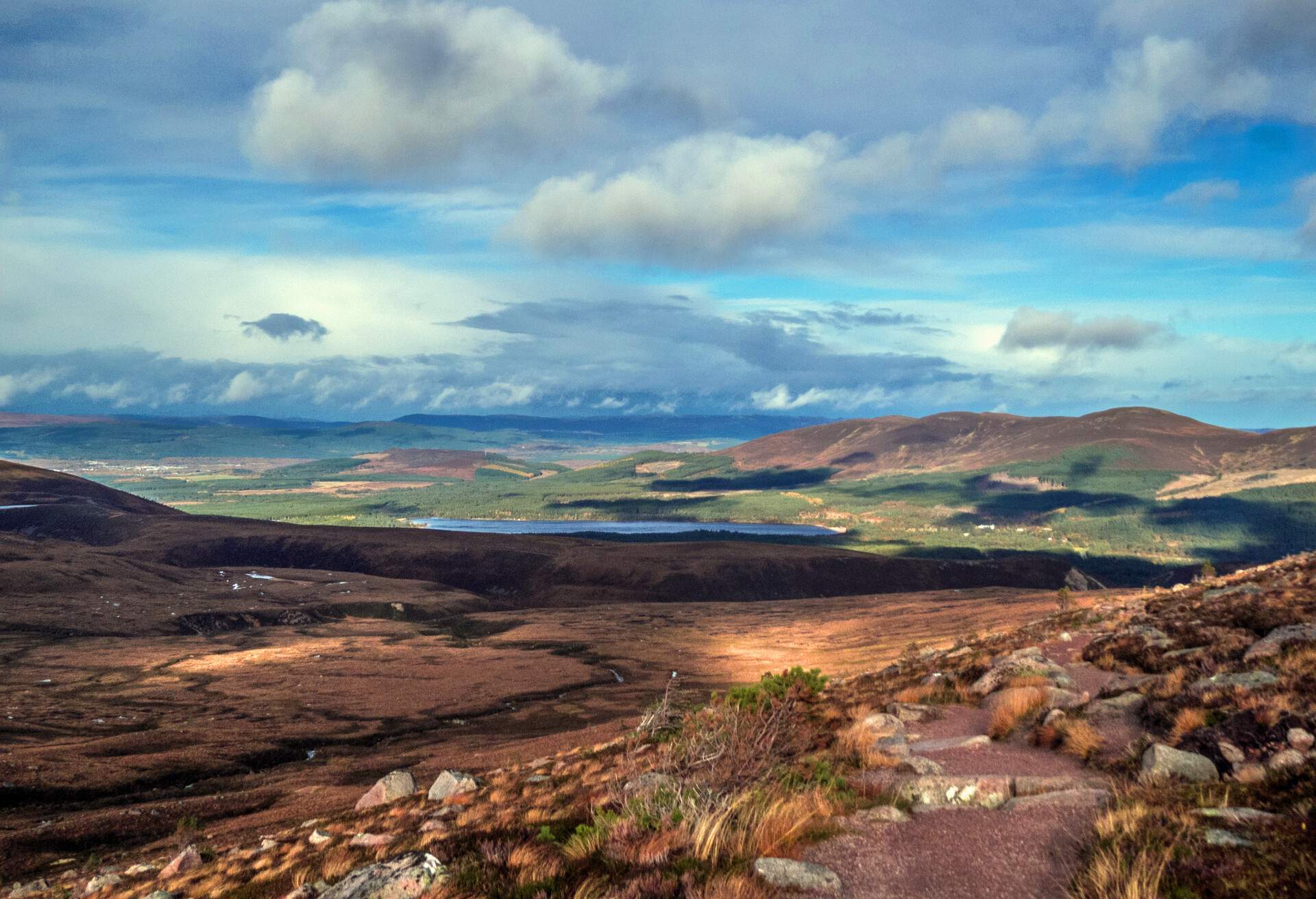 A contrasting landscape featuring barren land, a majestic mountain range, and rolling hills, set against a backdrop of cloudy blue sky.