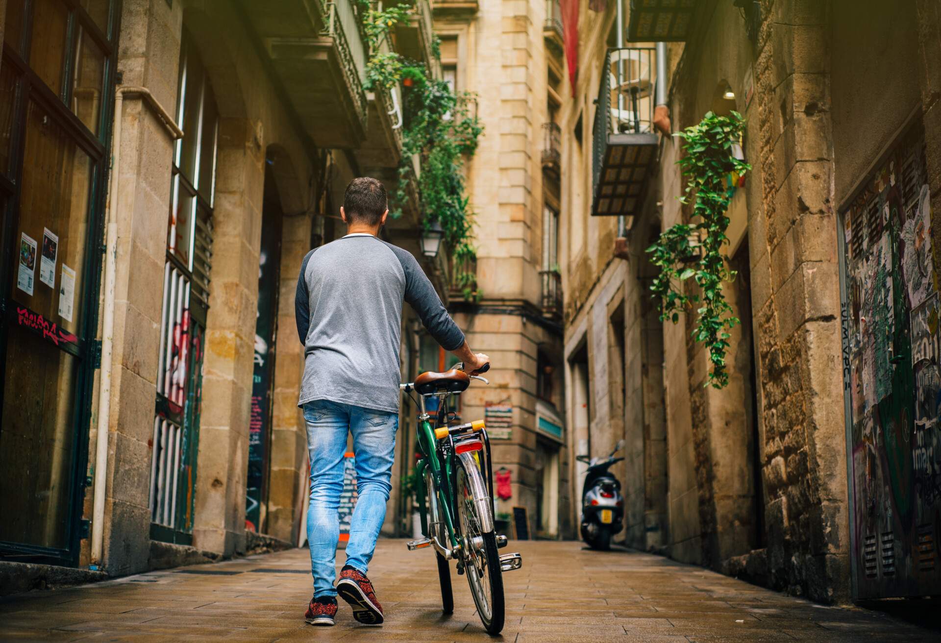 A man walking his bike along an alley between old buildings.