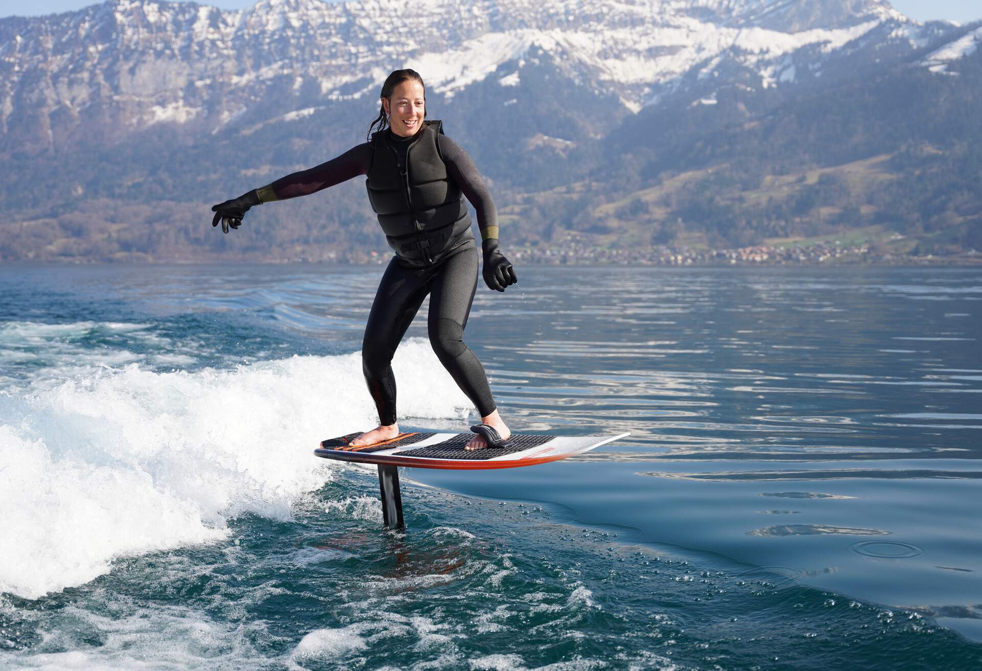 She surfs the wake behind boat in Lake Thun, Swiss Alps behind