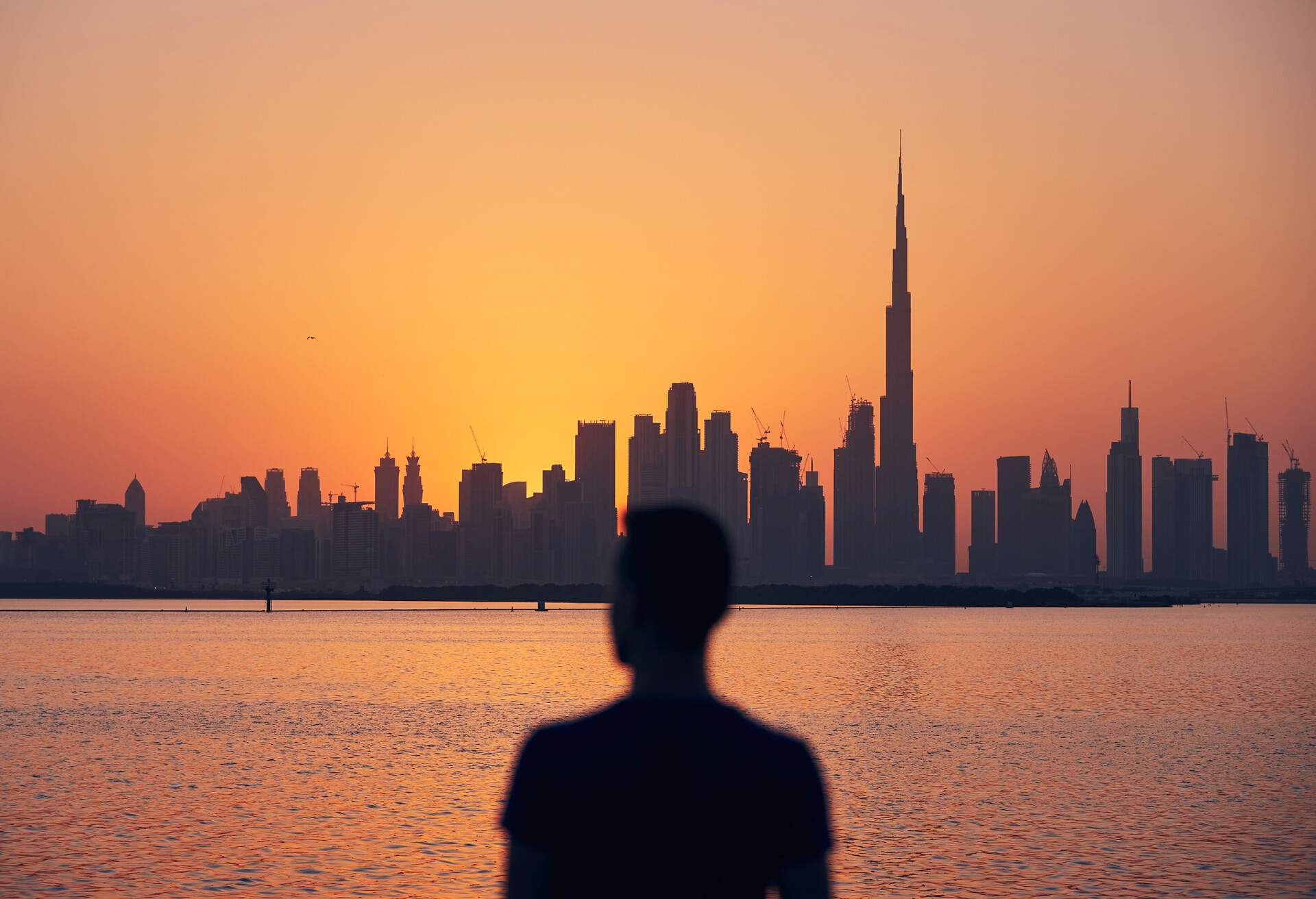 Silhouette of lonely man looking at cityscape at beautiful dusk. Urban skyline with tallest skyscraper Burj Khalifa, Dubai, United Arab Emirates.
