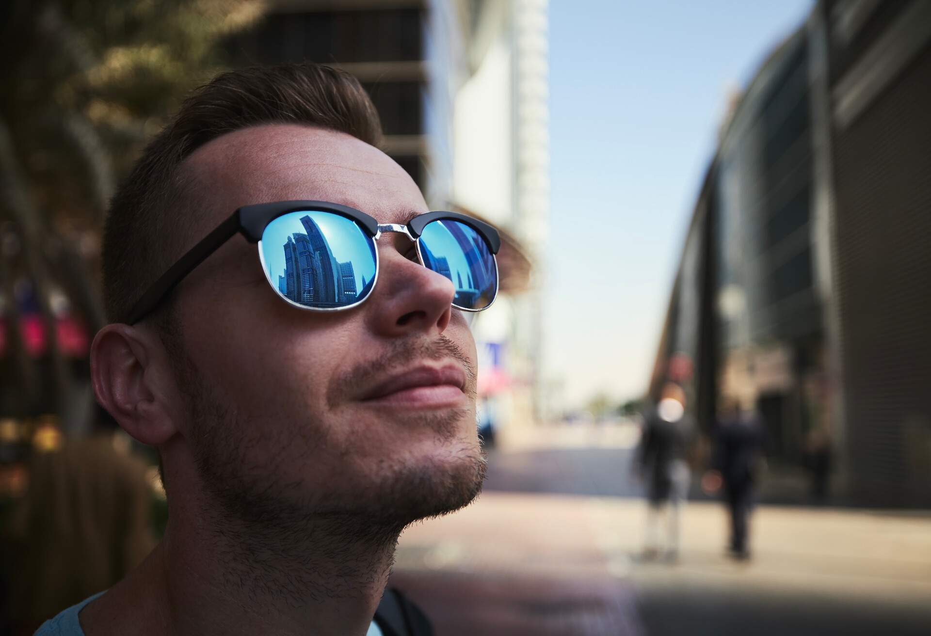 Reflection of skyscrapers in sunglasses. Portrait of young man on city street. Traveler in Dubai, United Arab Emirates.