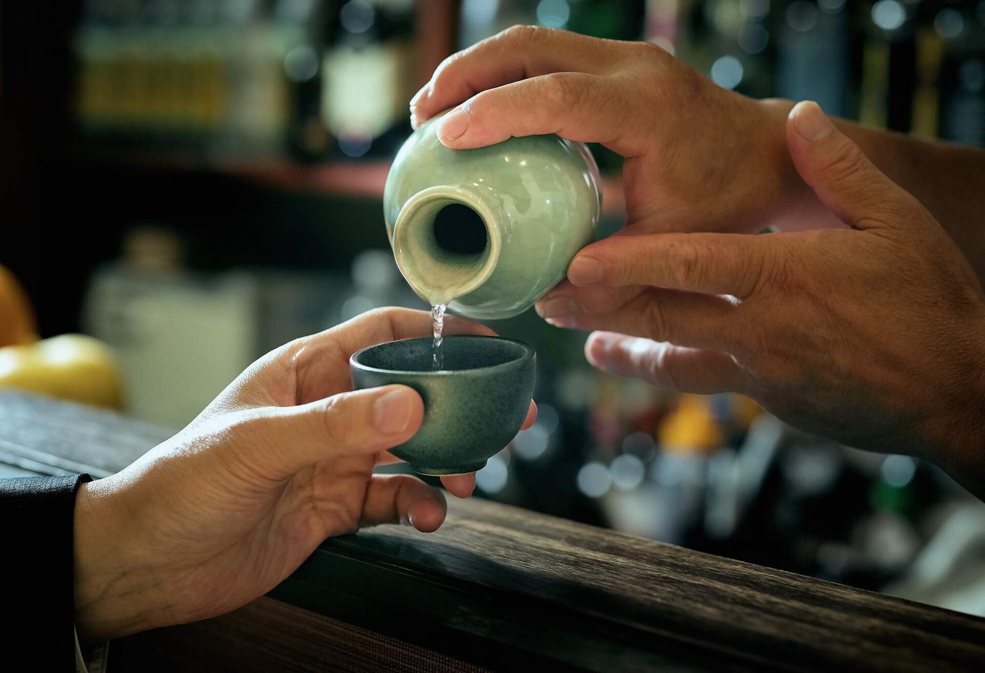 An individual pouring clear liquor into traditional sake cup, Shinjuku TOKYO