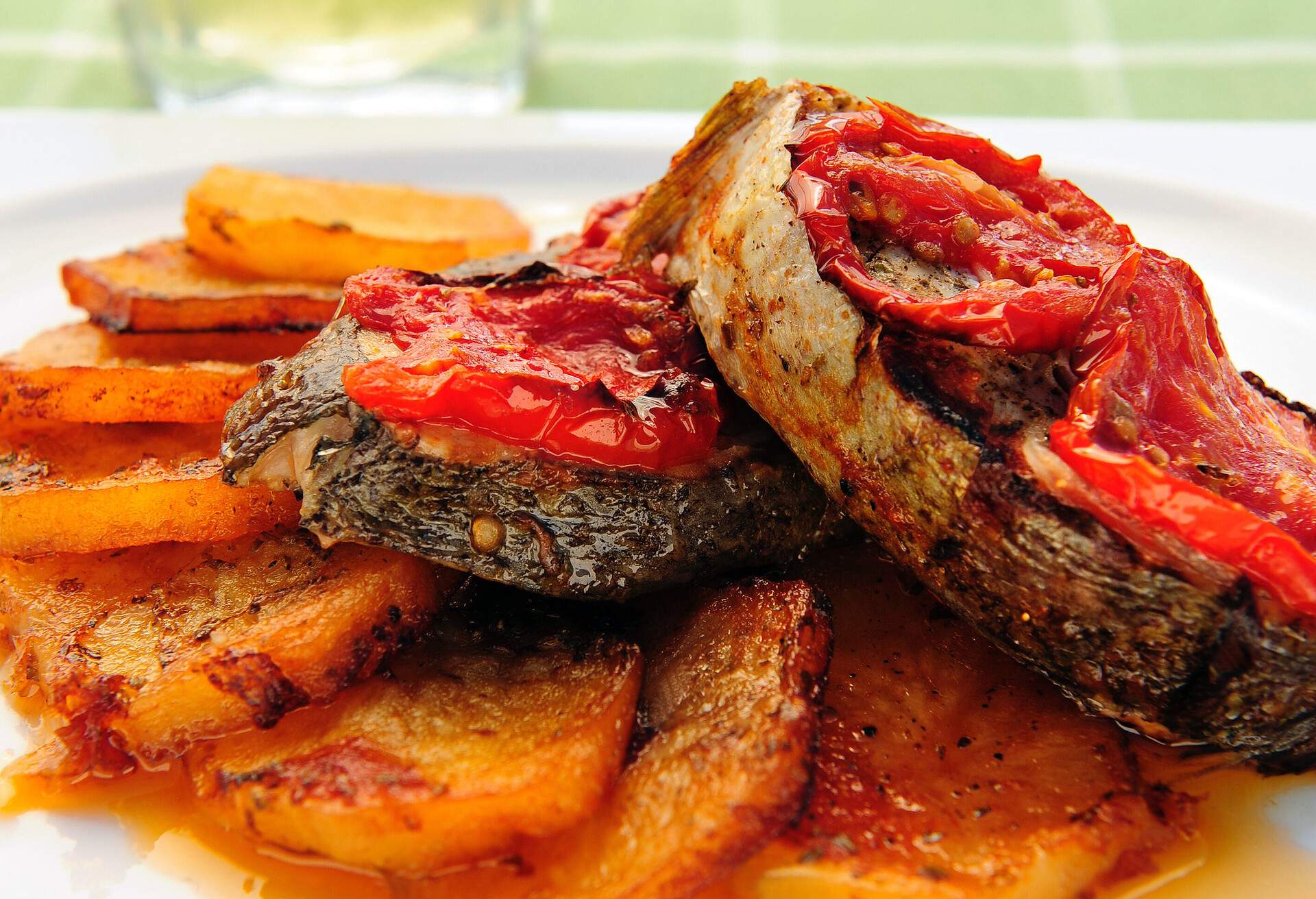 a plate of fish with baked potatoes in tomato sauce