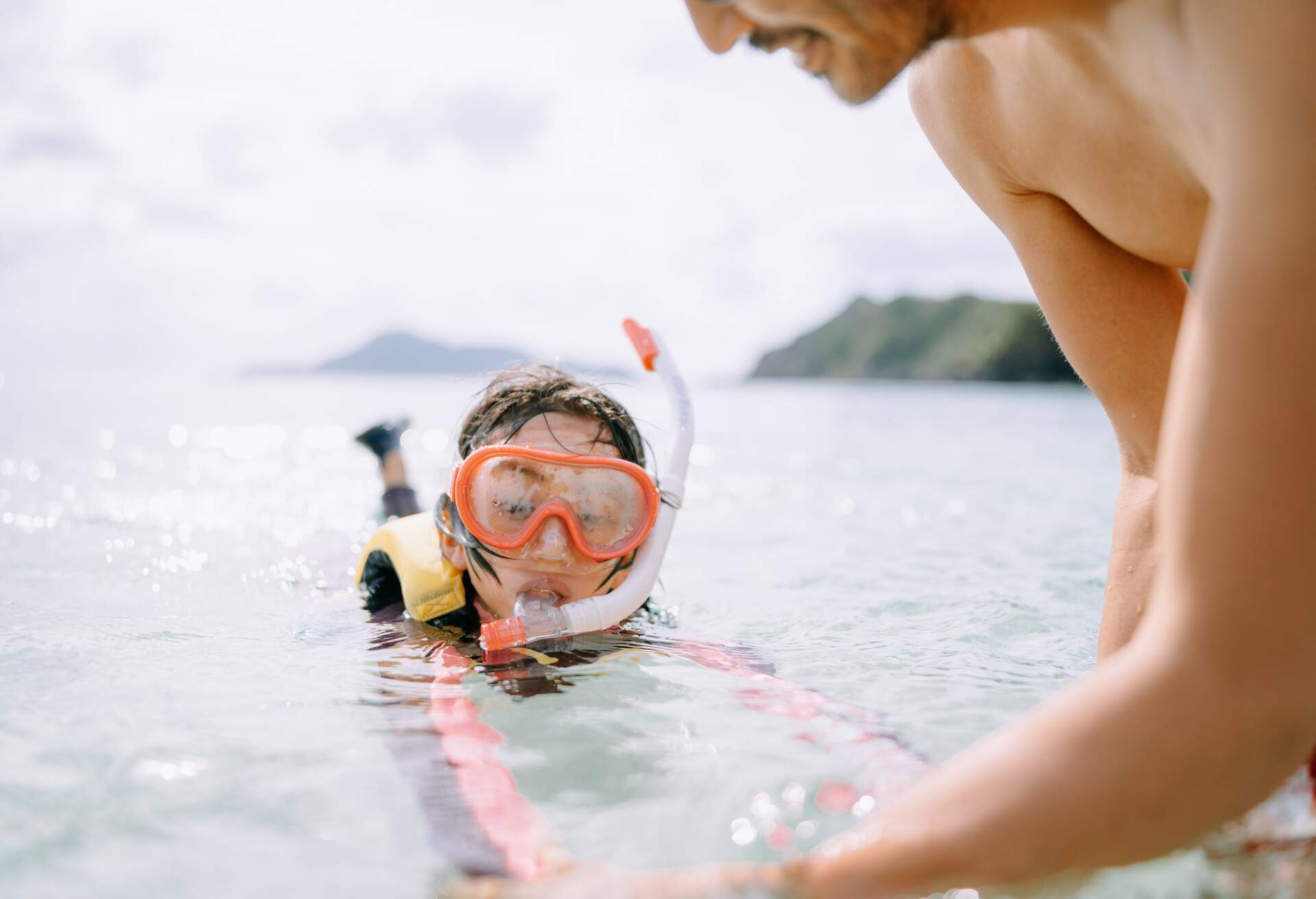 Father teaching his daughter how to snorkel in clear shallow water, Okinawa, Japan