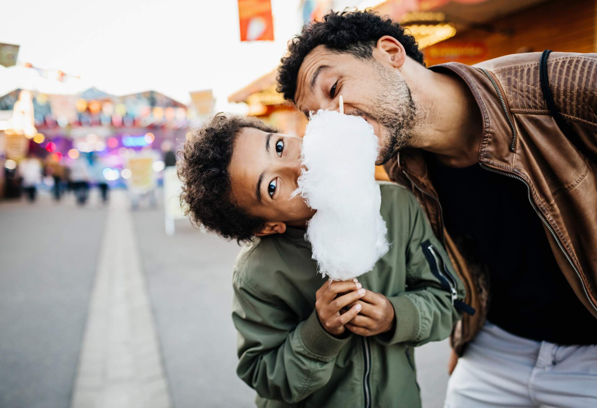A playful father and son sharing a bloom of candy floss while spending the day at the fun fair together.