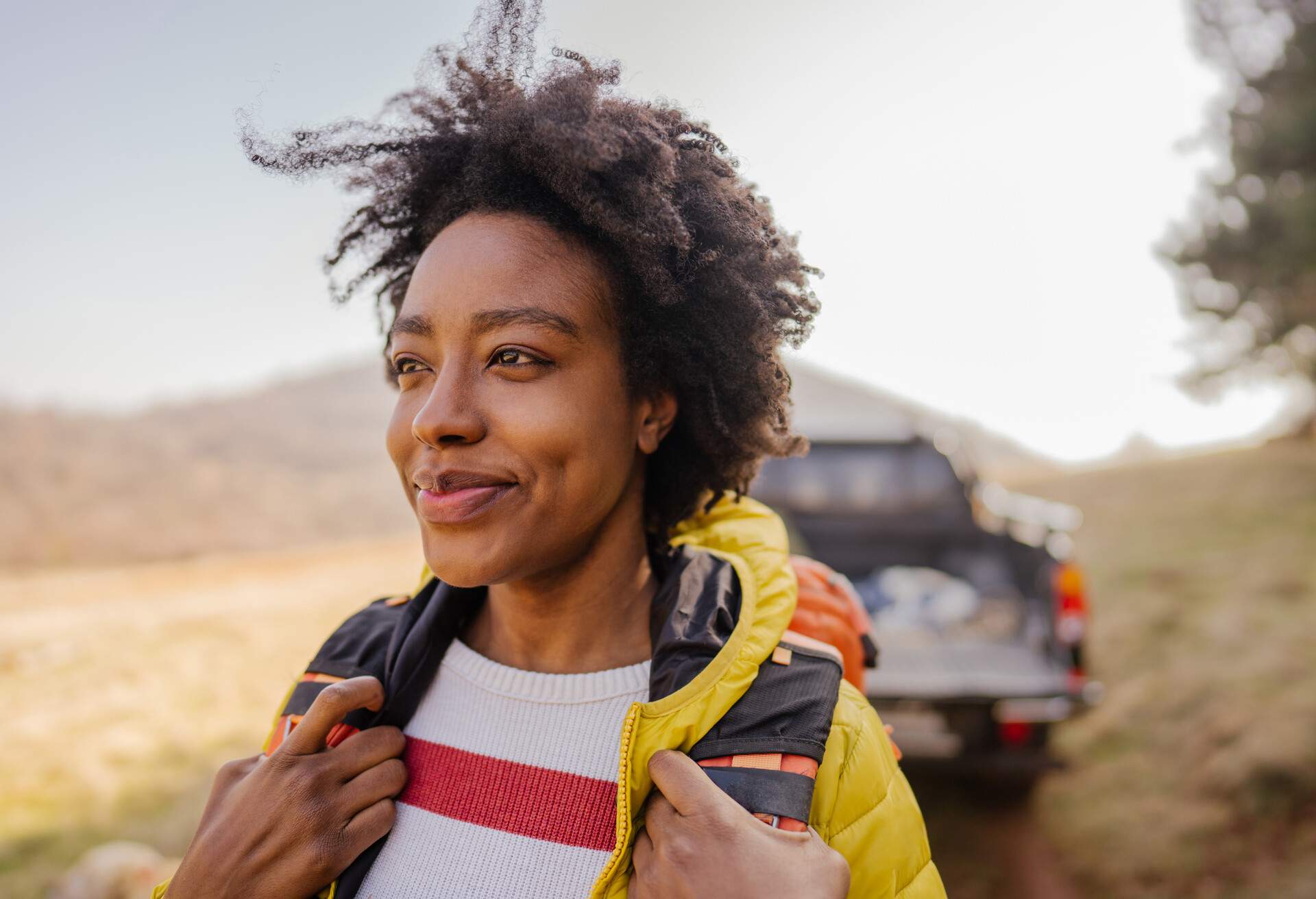 Photo of a young smiling woman carrying a backpack during the road trip