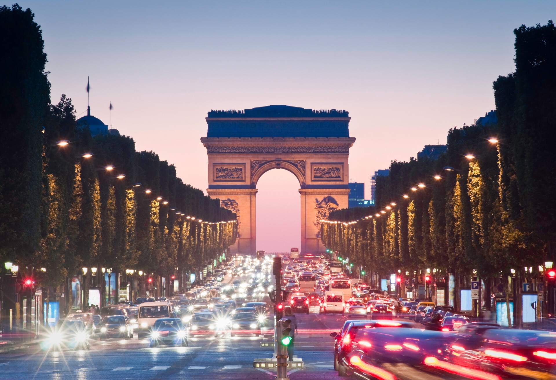 Evening traffic illuminating the Champs-Elysees Avenue with the Arc de Triomphe in the distance.