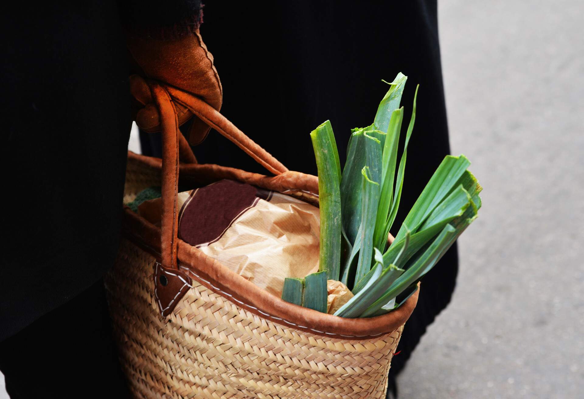 leek in a straw bag in the hands of a woman