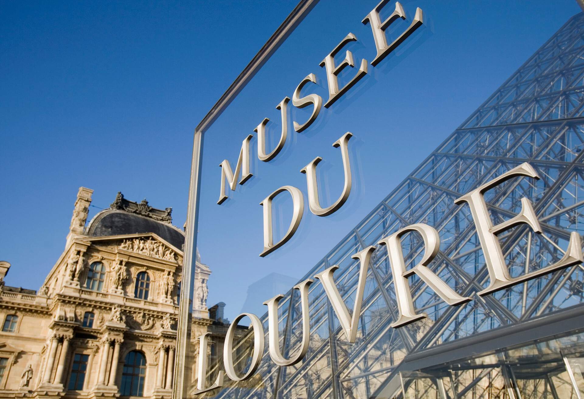 The upper portion of the Louvre palace, including a portion of the Louvre Pyramid and a "Musee du Louvre" sign.