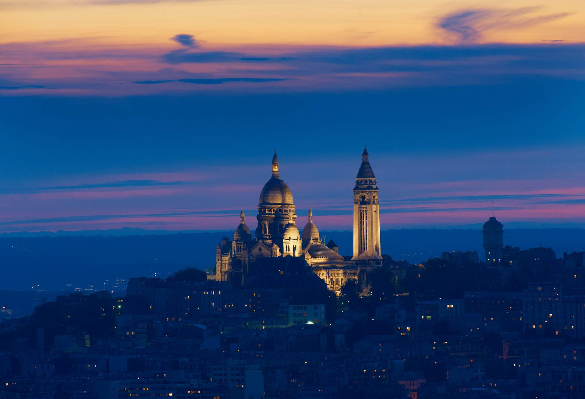 Illuminated church of Sacre Coeur in Paris at dusk surrounded by buildings