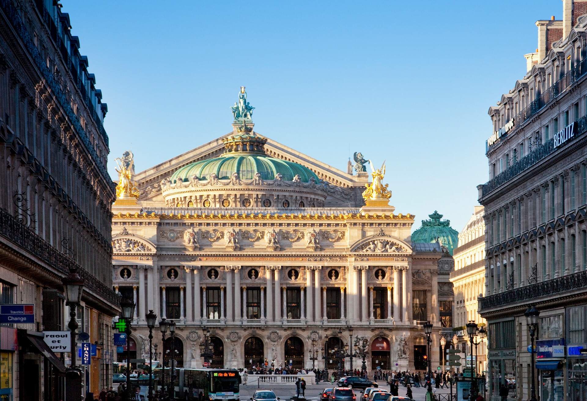 A large edifice with a dome cap and an elaborately sculpted front was topped with three statues, one on each corner and one on the dome cap, facing the busy street.