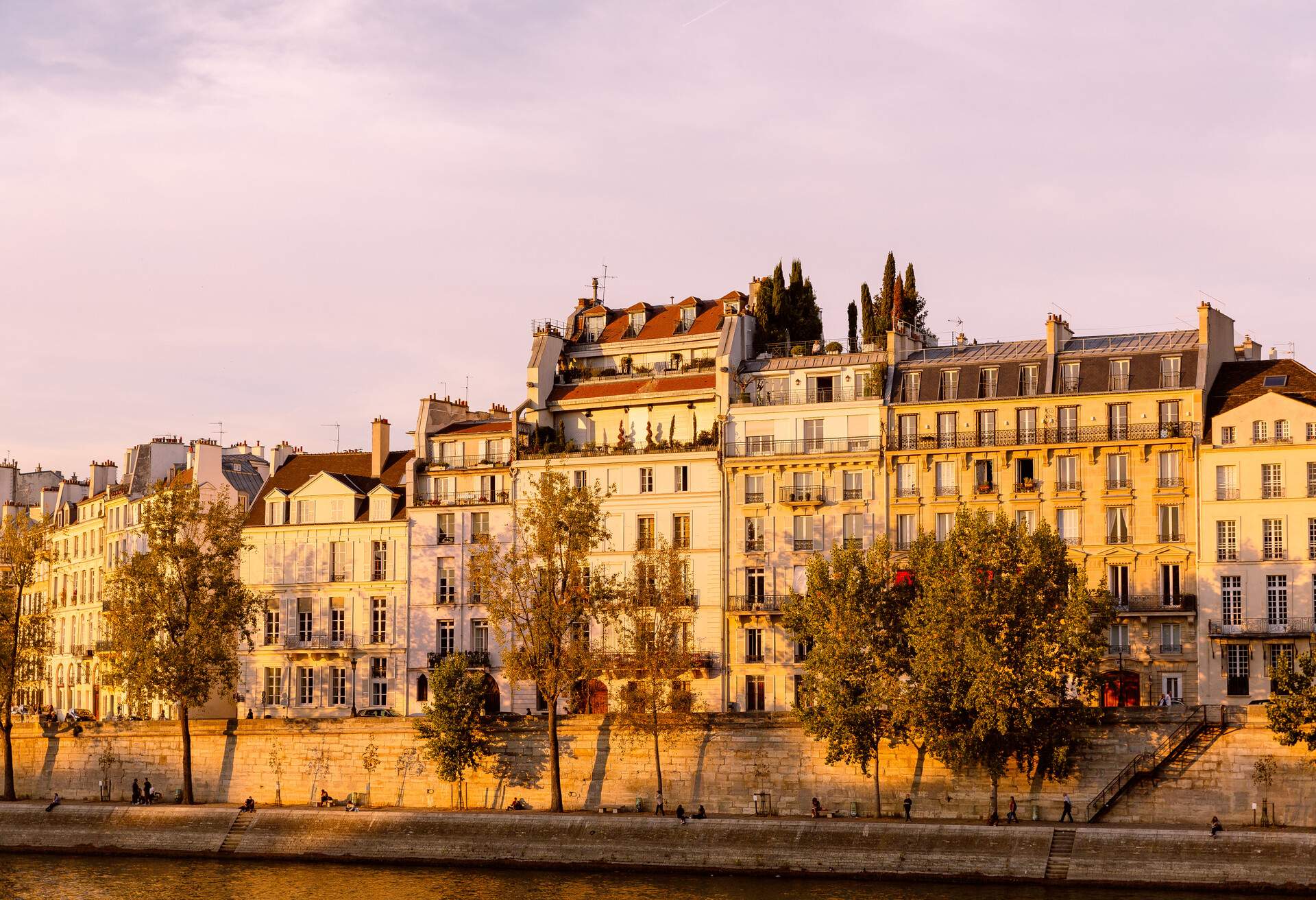 Haussmann-style buildings with wrought iron balconies along a boulevard by the river.