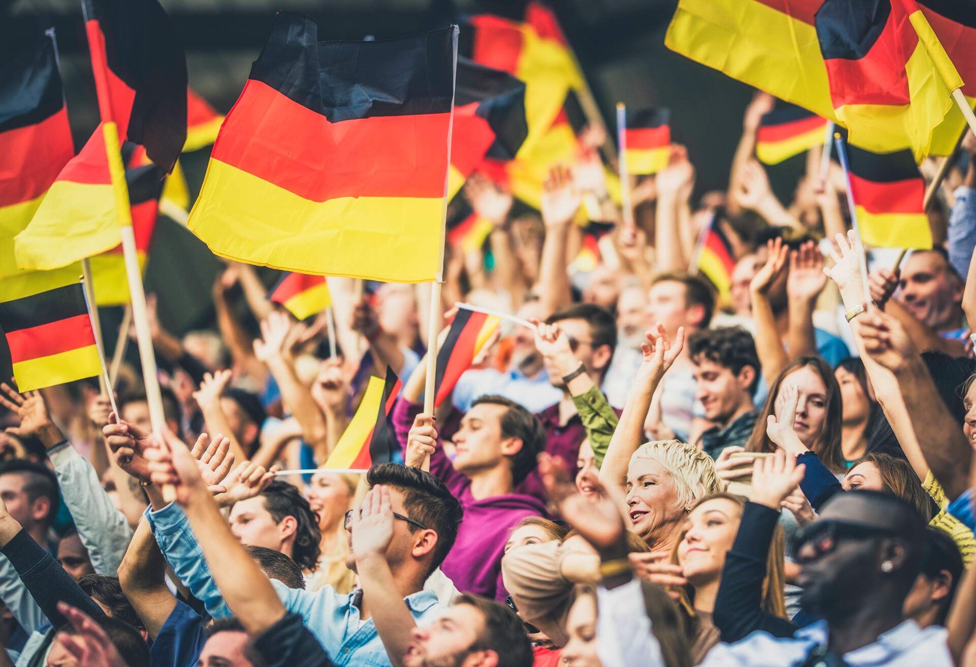 Large group of people waving Germany flags while standing on stadium bleachers.