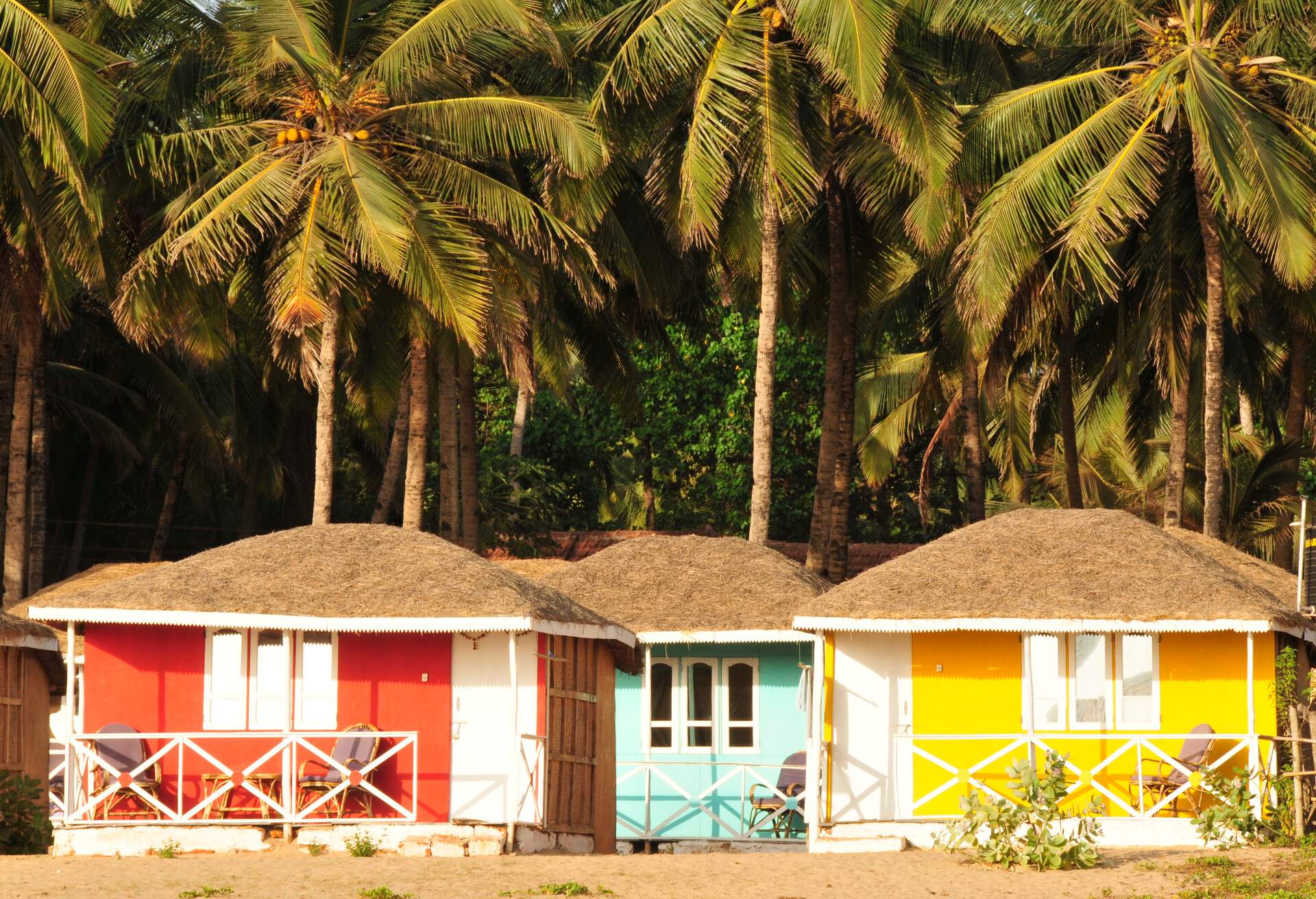 Colourful beach huts cluster under the lush palm trees.
