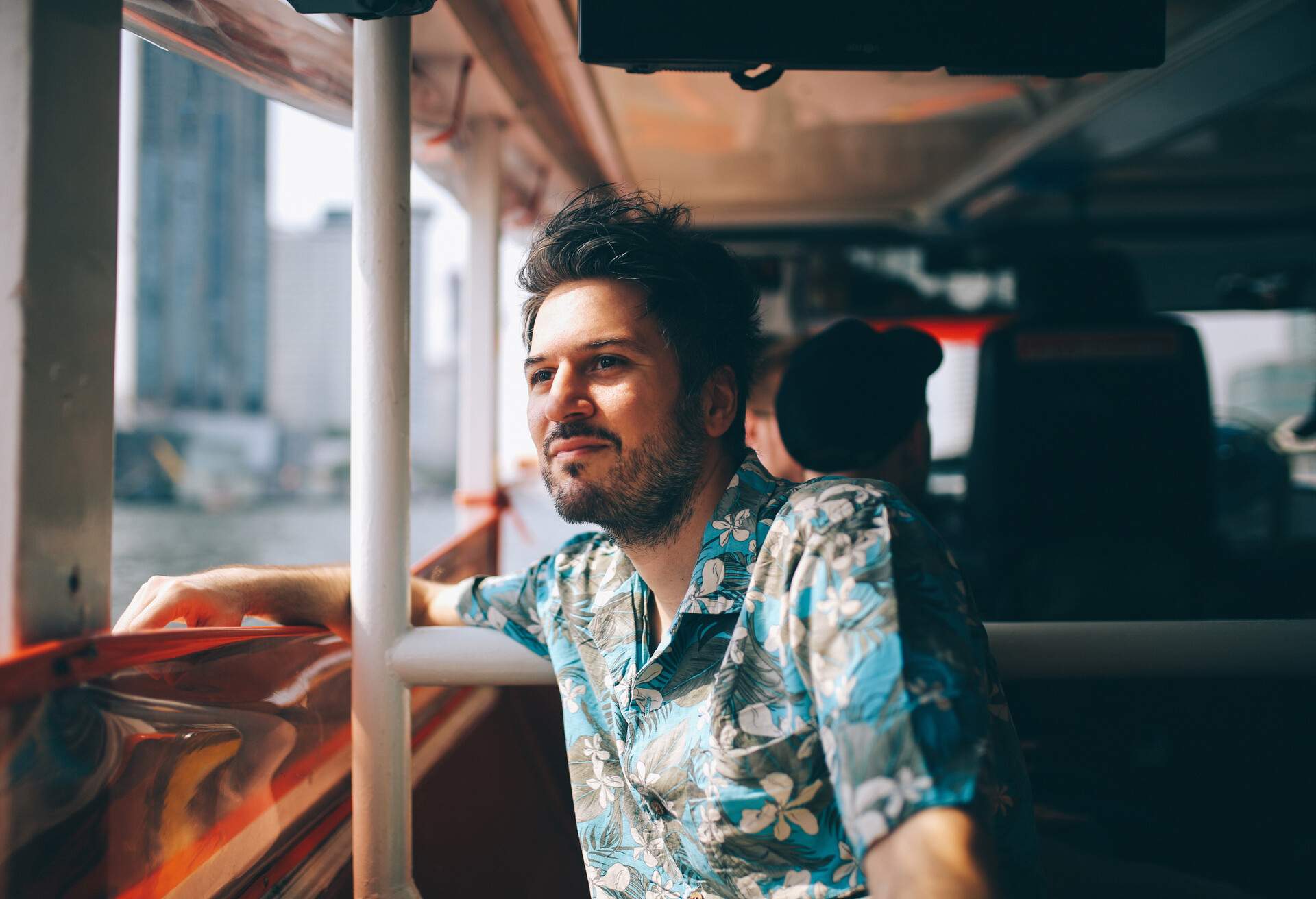 A man dressed in a blue Hawaiian shirt admiring the scenery from a ferry boat.
