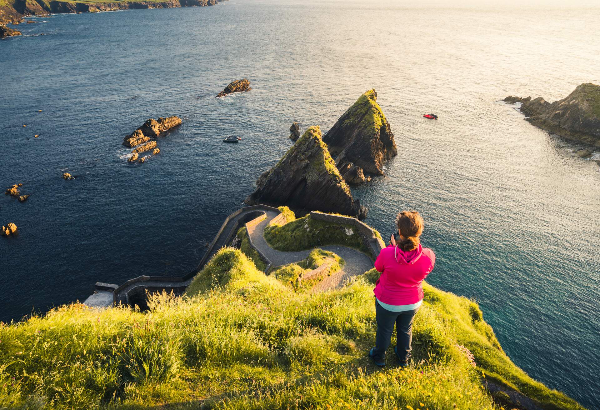 Republic of Ireland, Munster province, County Kerry: high angle view of a woman taking pictures at Dunquin Pier, along the Ring of Kerry on Dingle Peninsula.