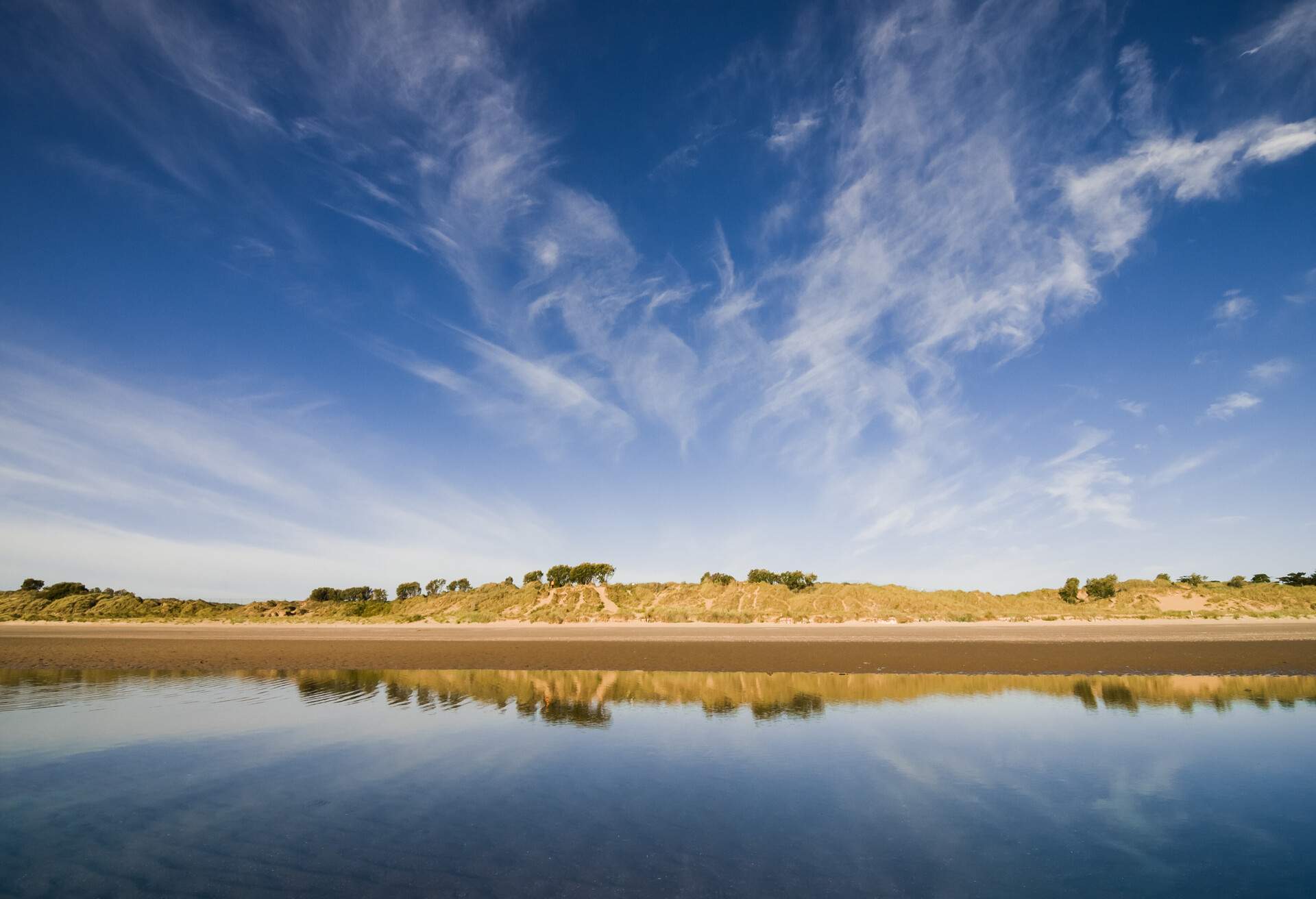 Wide angle view of sand dunes in Portmarnock. Photographed at low tide with large tide pool reflecting the dunes or 'Velvet Strand' at it's known. Blue sky with some light cloud that seems to rise like steam from the land.