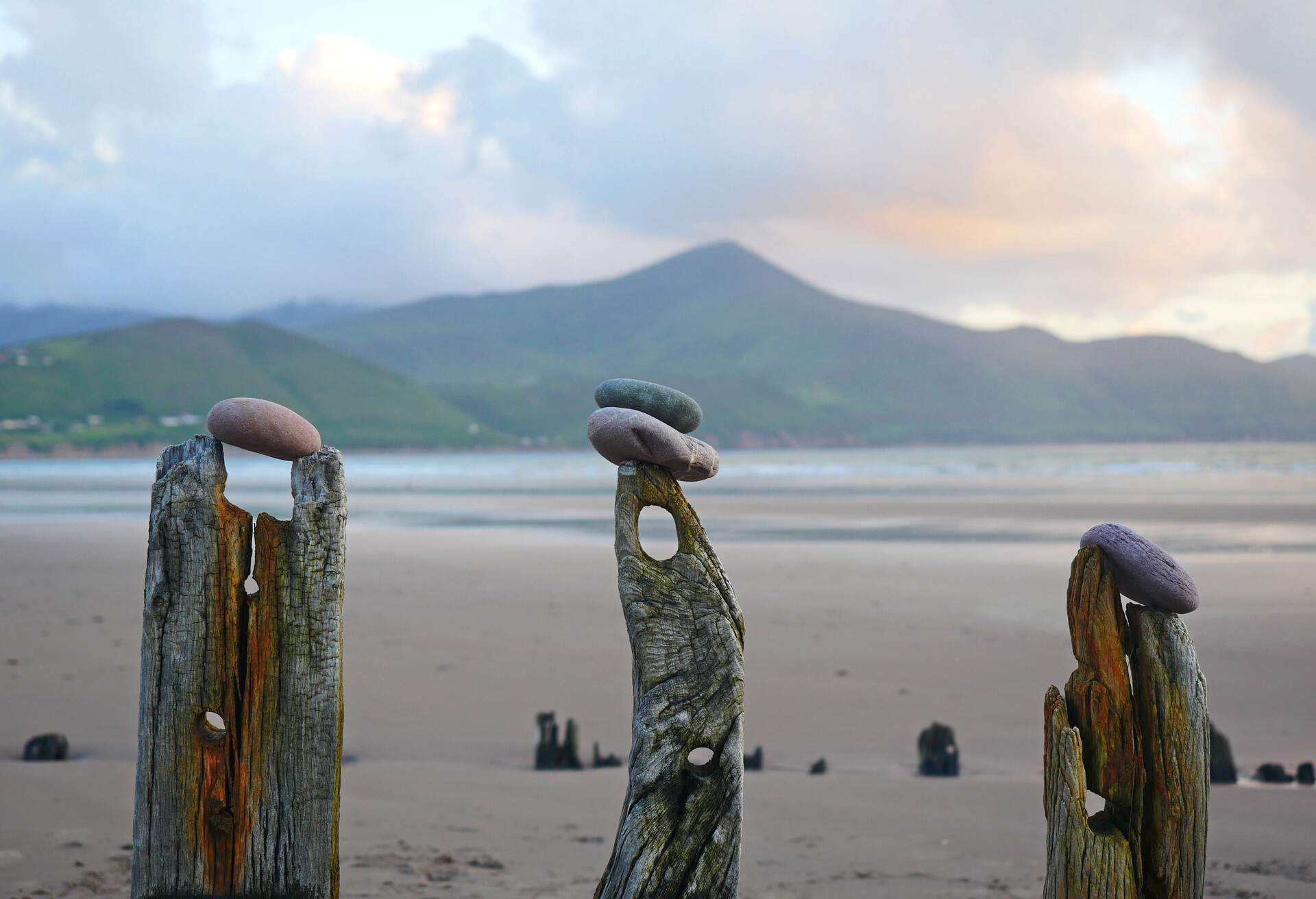 Pebbles balancing on 3 stumps of wood from a shipwreck on Rossbeigh beach, Ireland with Seefin Mountain in the distance.