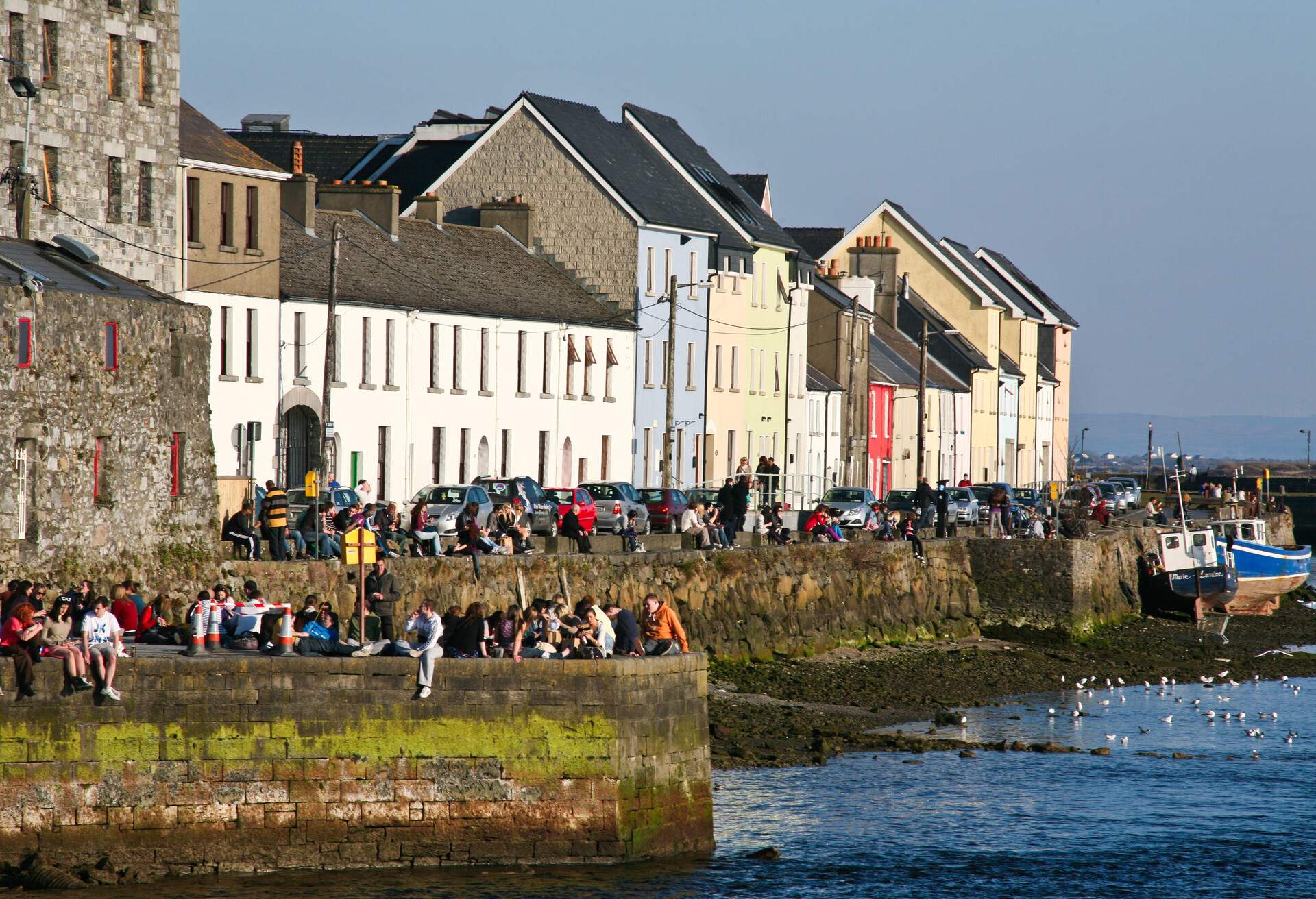 People enjoying the sunshine sitting on the quays at the Cladagh, Galway City, Ireland.