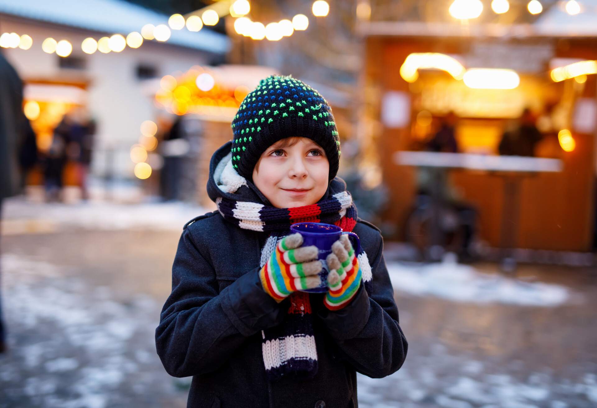 Little cute kid boy drinking hot children punch or chocolate on German Christmas market. Happy child on traditional family market in Germany, Laughing boy in colorful winter clothes.