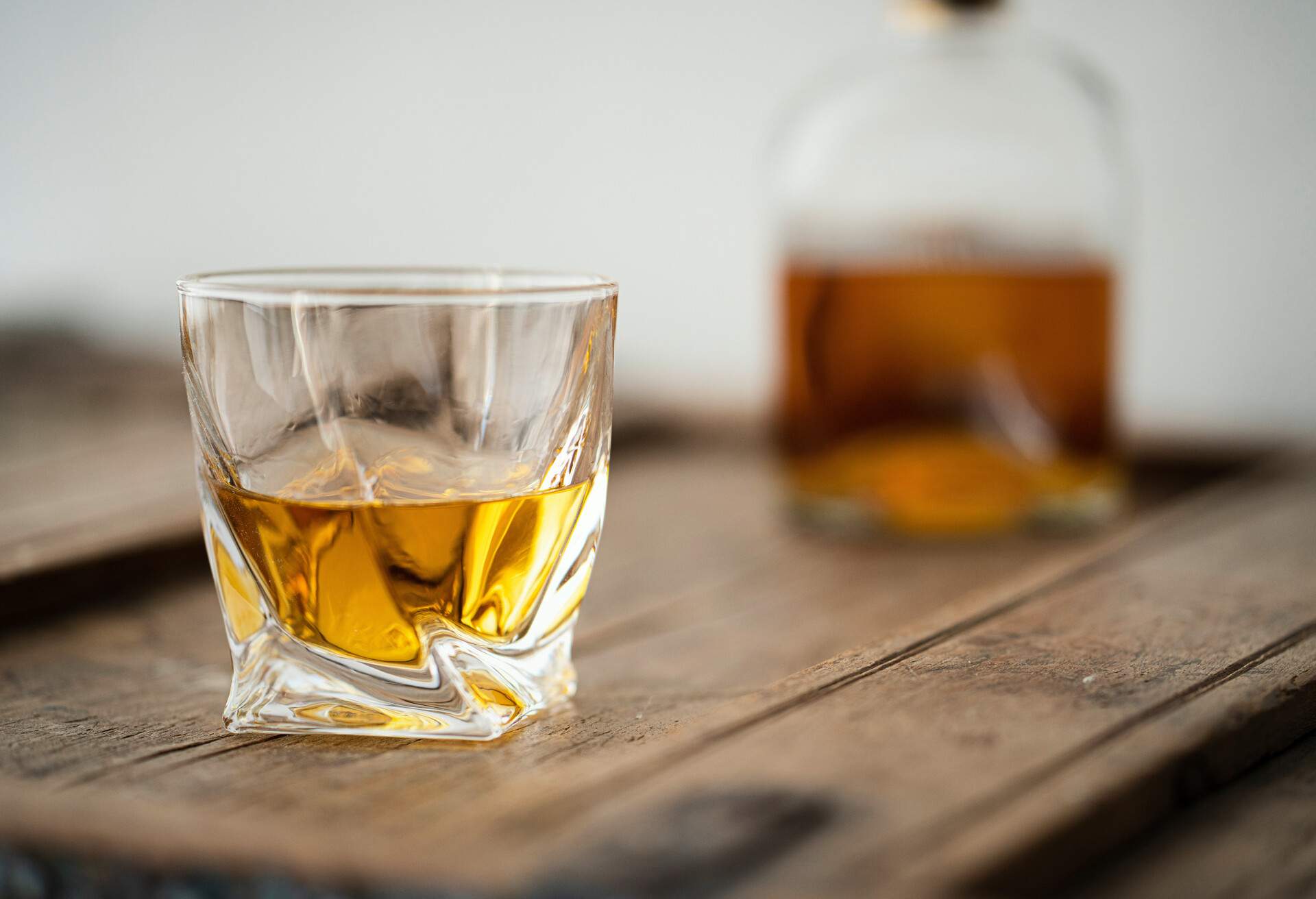 Whisky glass and bottle with golden shimmering scotch on a brown used shabby barrel, white background