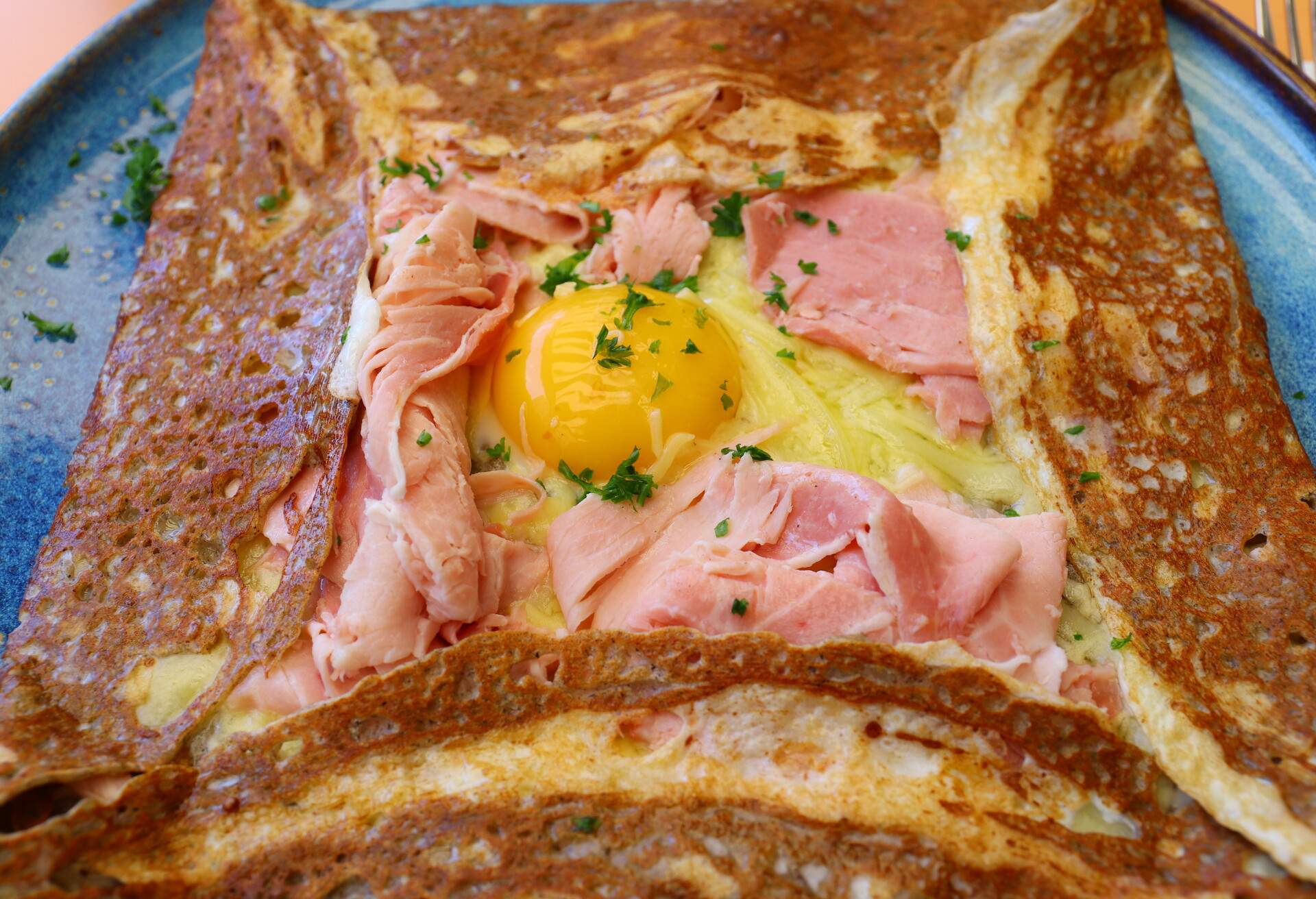 A closeup of a classic french crepes folded as a square with ham and an egg in the middle of the plate
