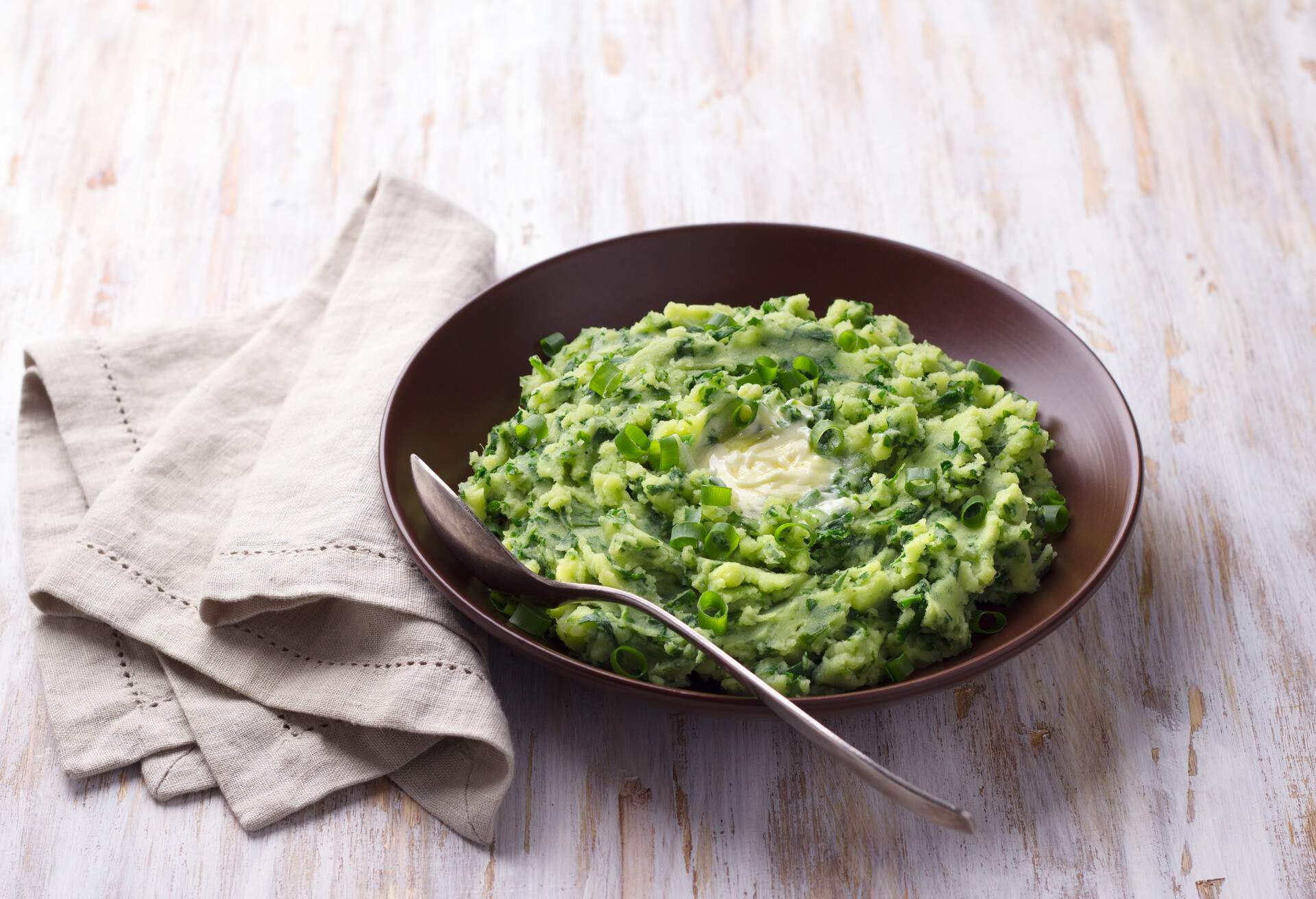 Colcannon, mashed potatoes with cale cabbage and green onions, traditional Irish dish, on a light wooden background