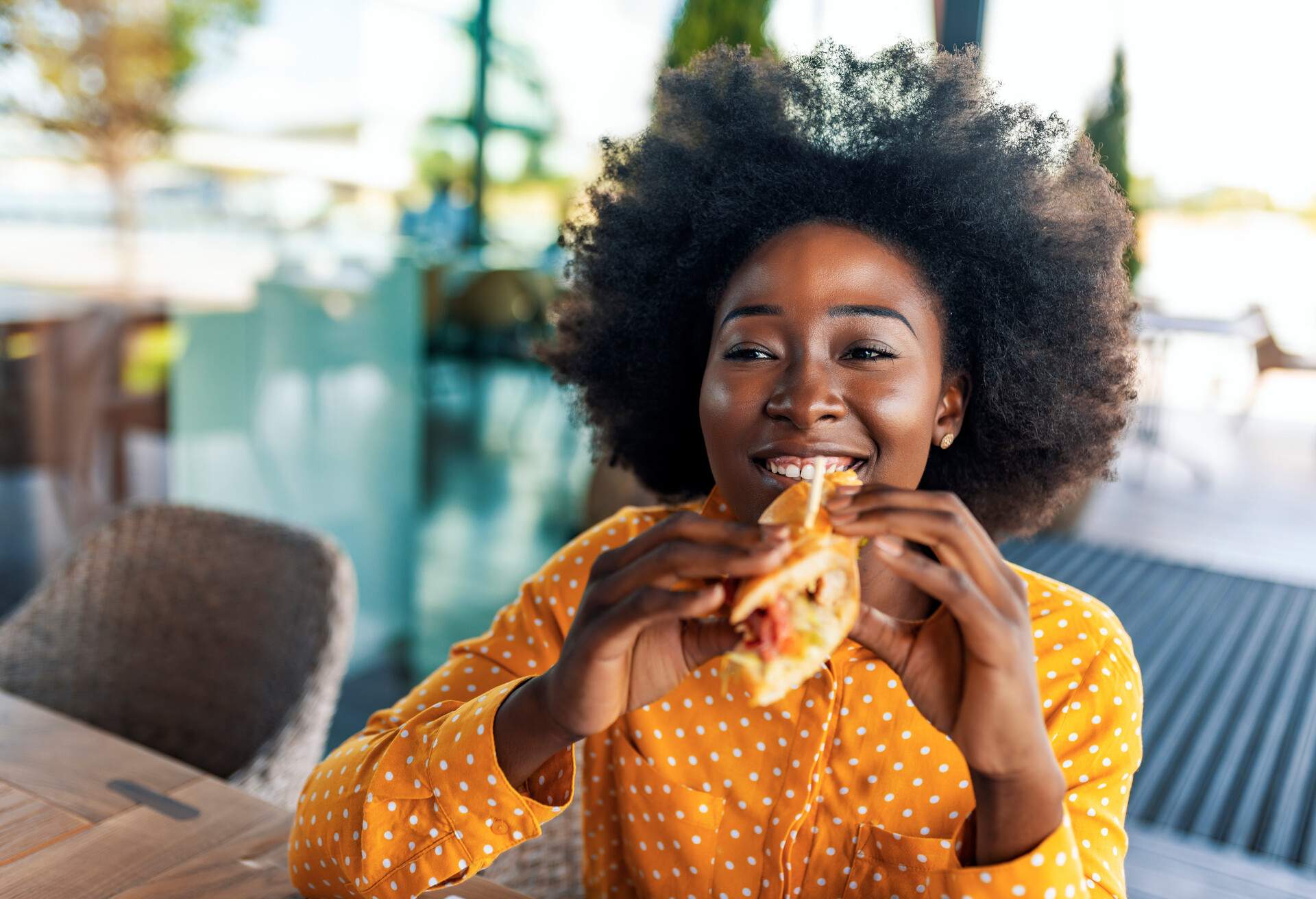 Girl bites off veggie sandwich. Copy space. Blurred background. Photo of young African woman eating sandwich at cafe.