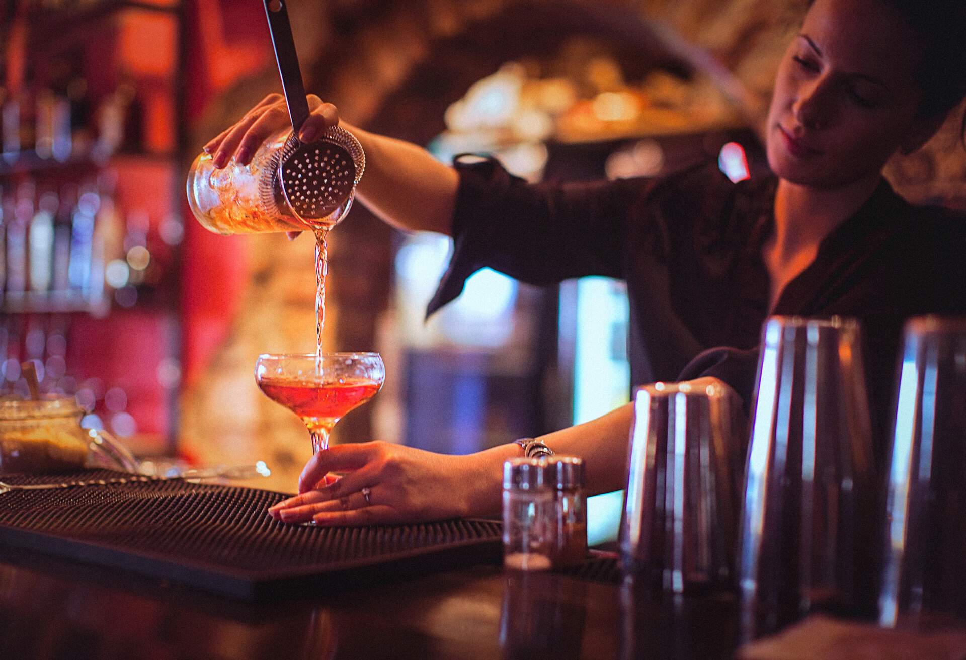 A bartender pouring a cocktail at the counter of a bar