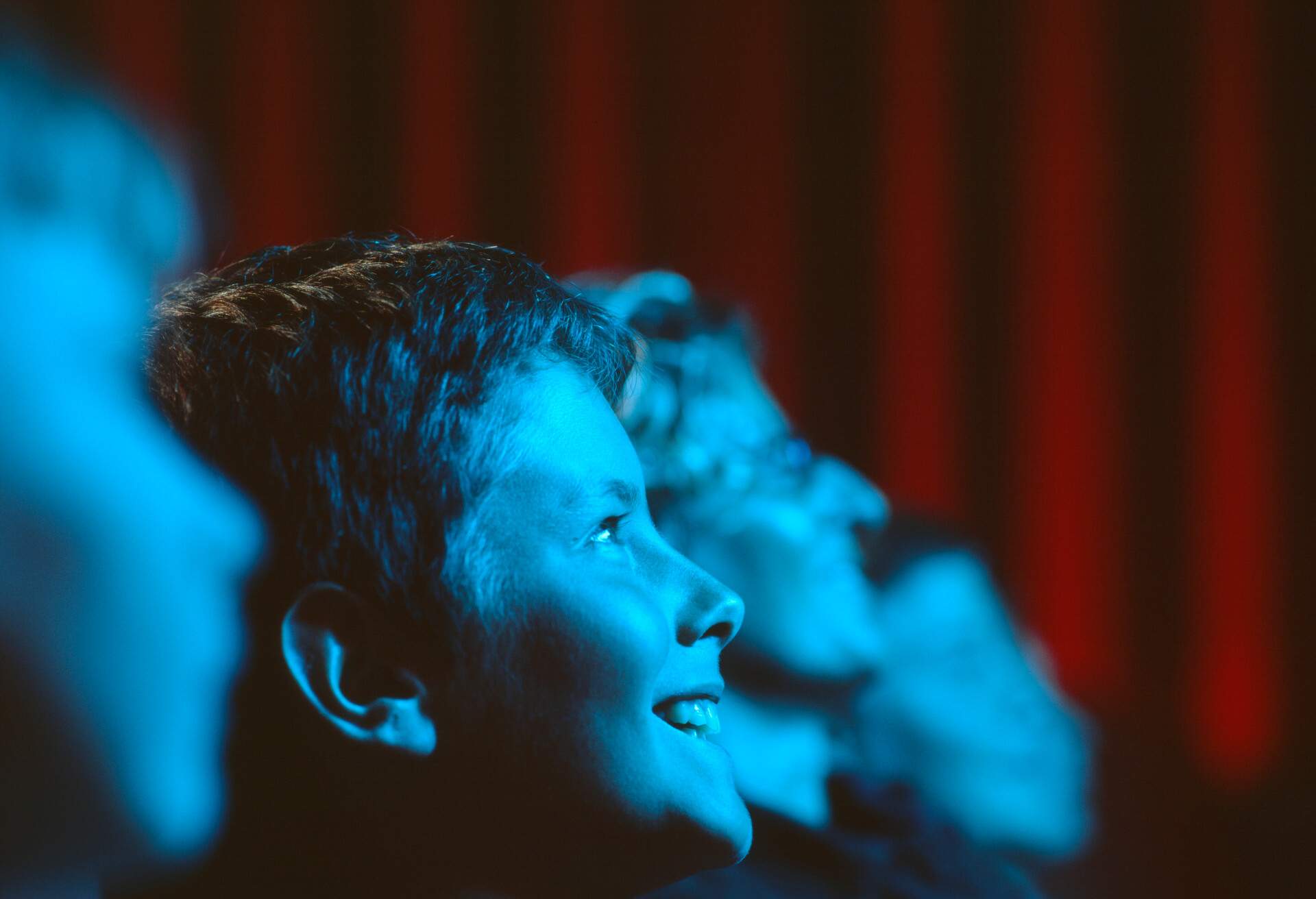 A closeup of a laughing boy in a blue light in the middle of an audience at a theatre