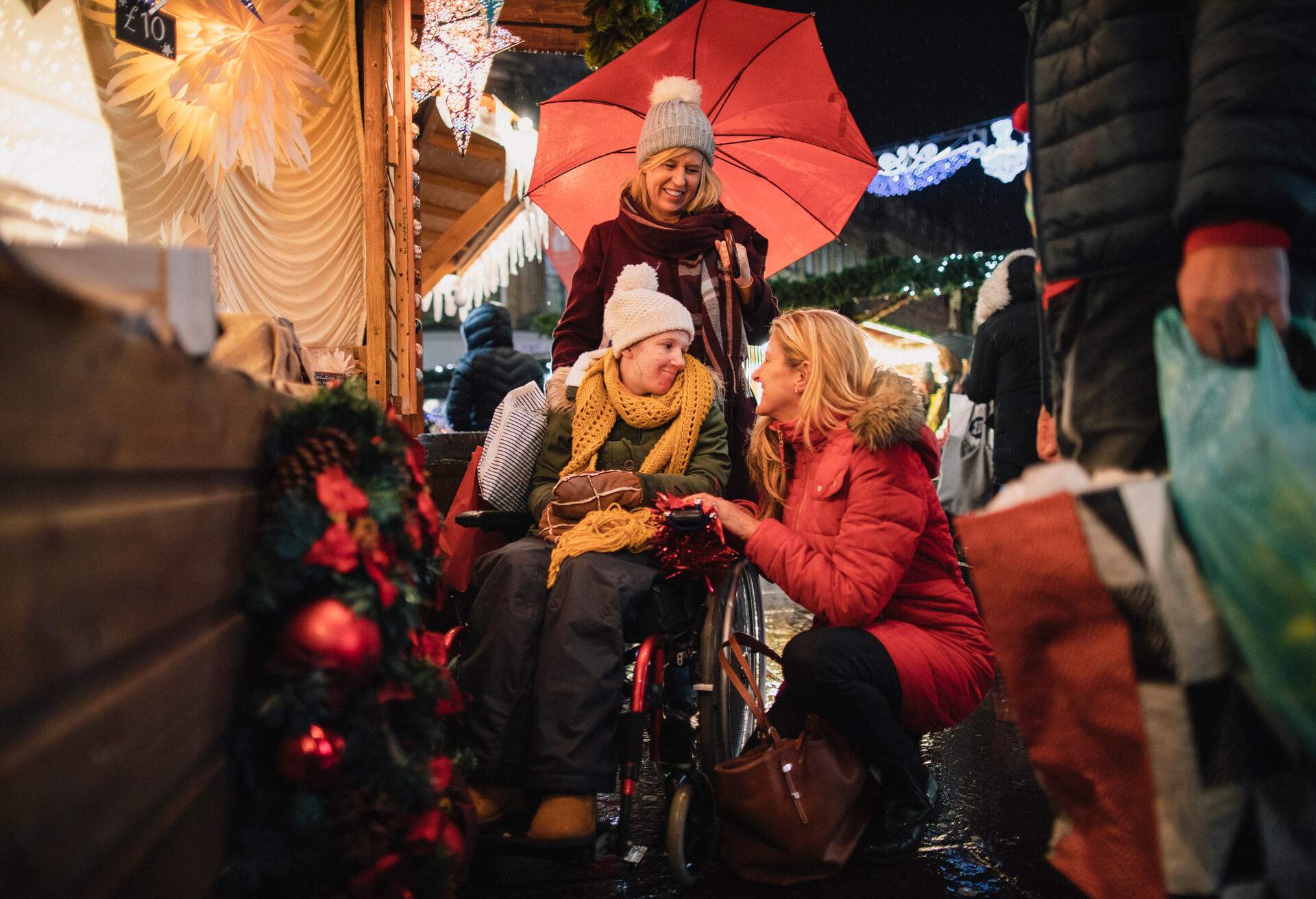 A side-view shot of a family buying sweet food from a small business Christmas market stall in the city, they are wearing warm clothing on a cold December​ night.