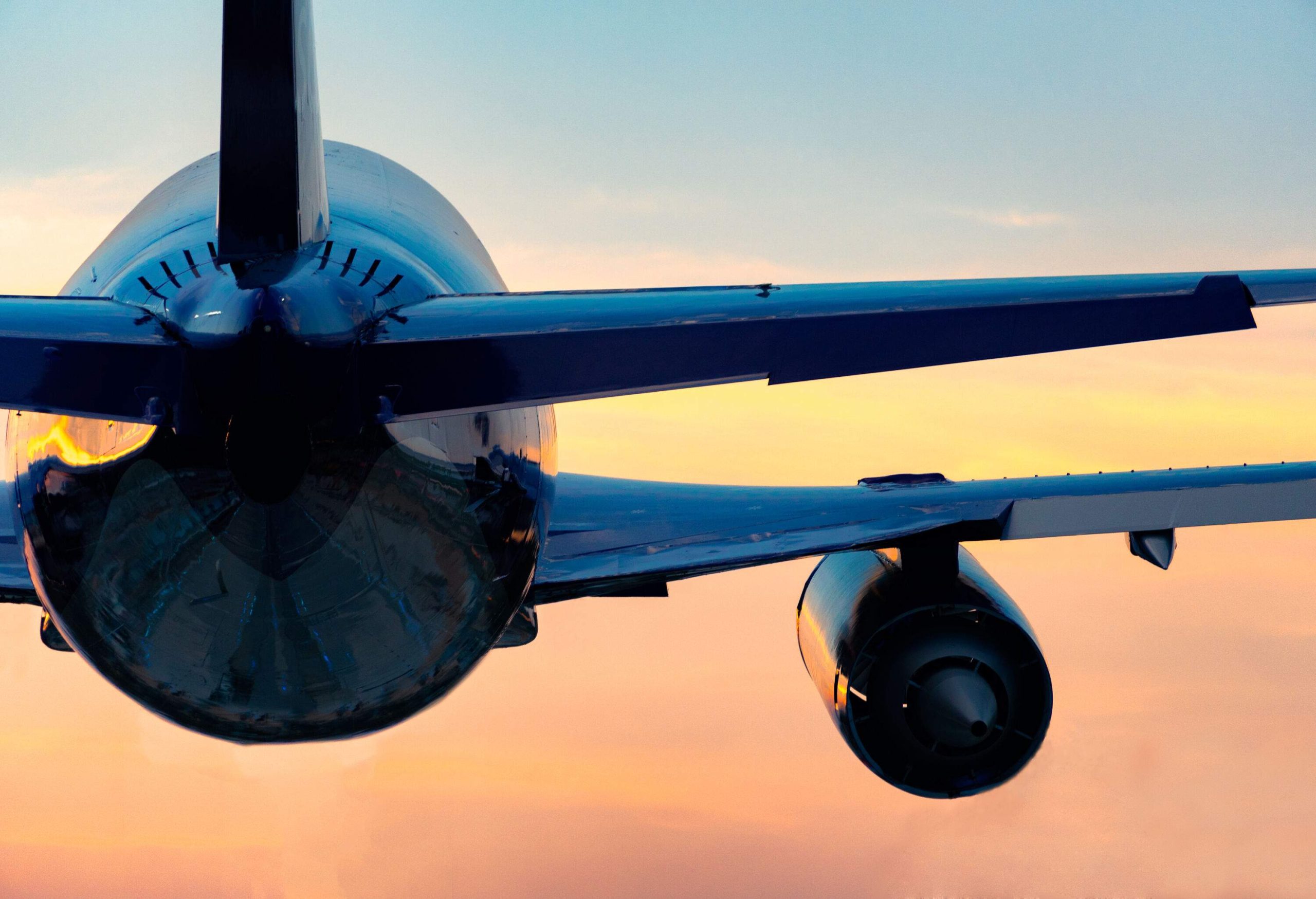 The backside of an airplane in flight against the backdrop of a sunset sky.