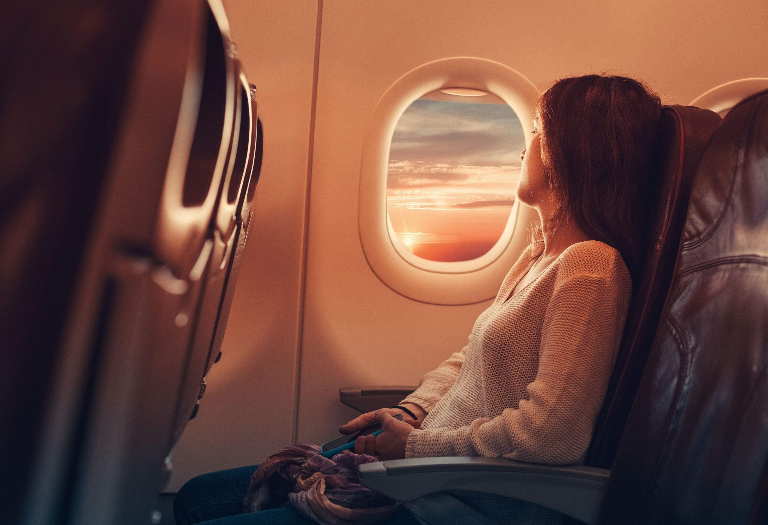 A woman in an airplane gazes through the window, her eyes captivated by the sight of fluffy clouds outside.