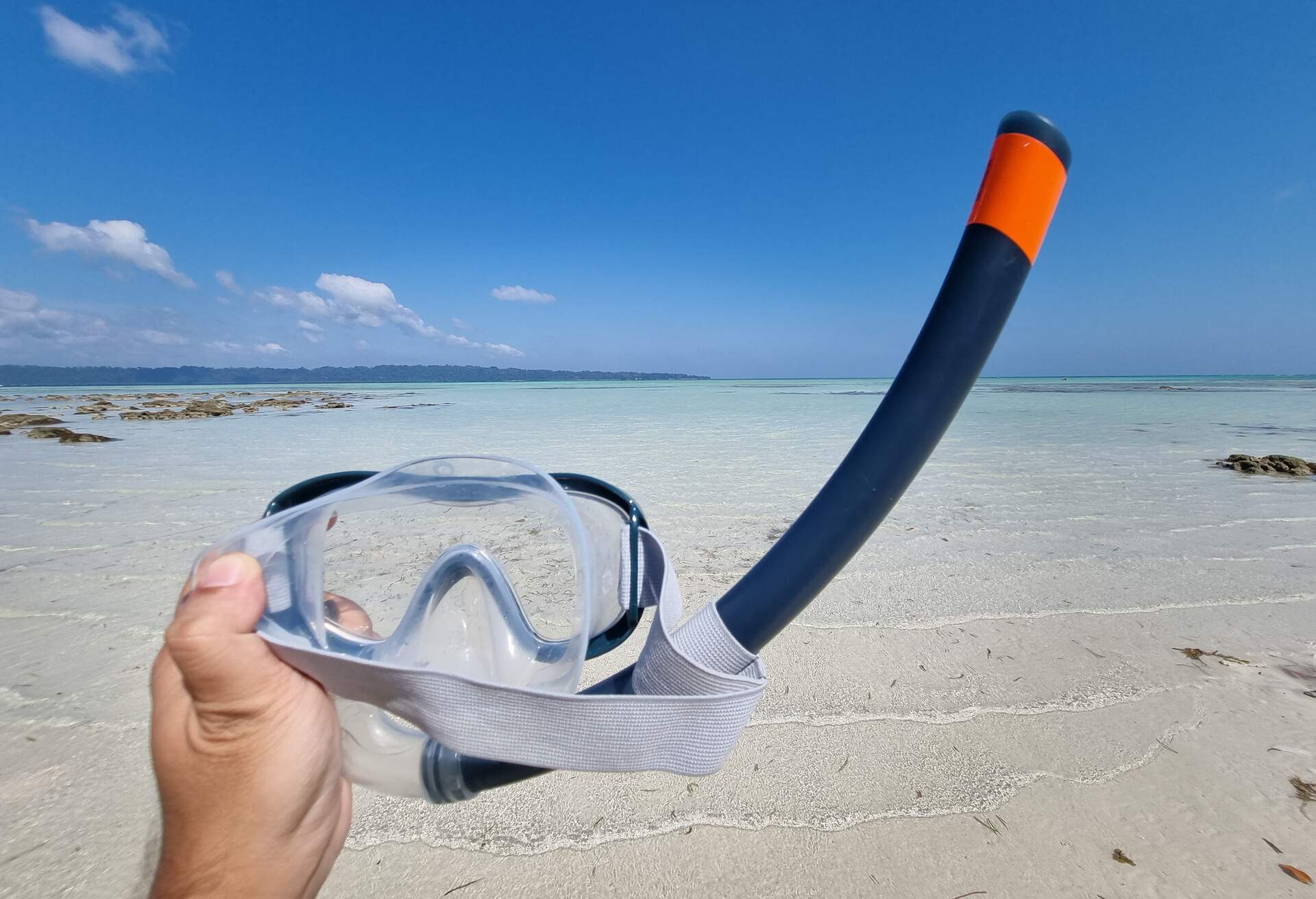 Panning shot holding out a snorkeling mask and breathing tube while going from the beach to the blue green waters at kala pathar beach andaman nicobar island India