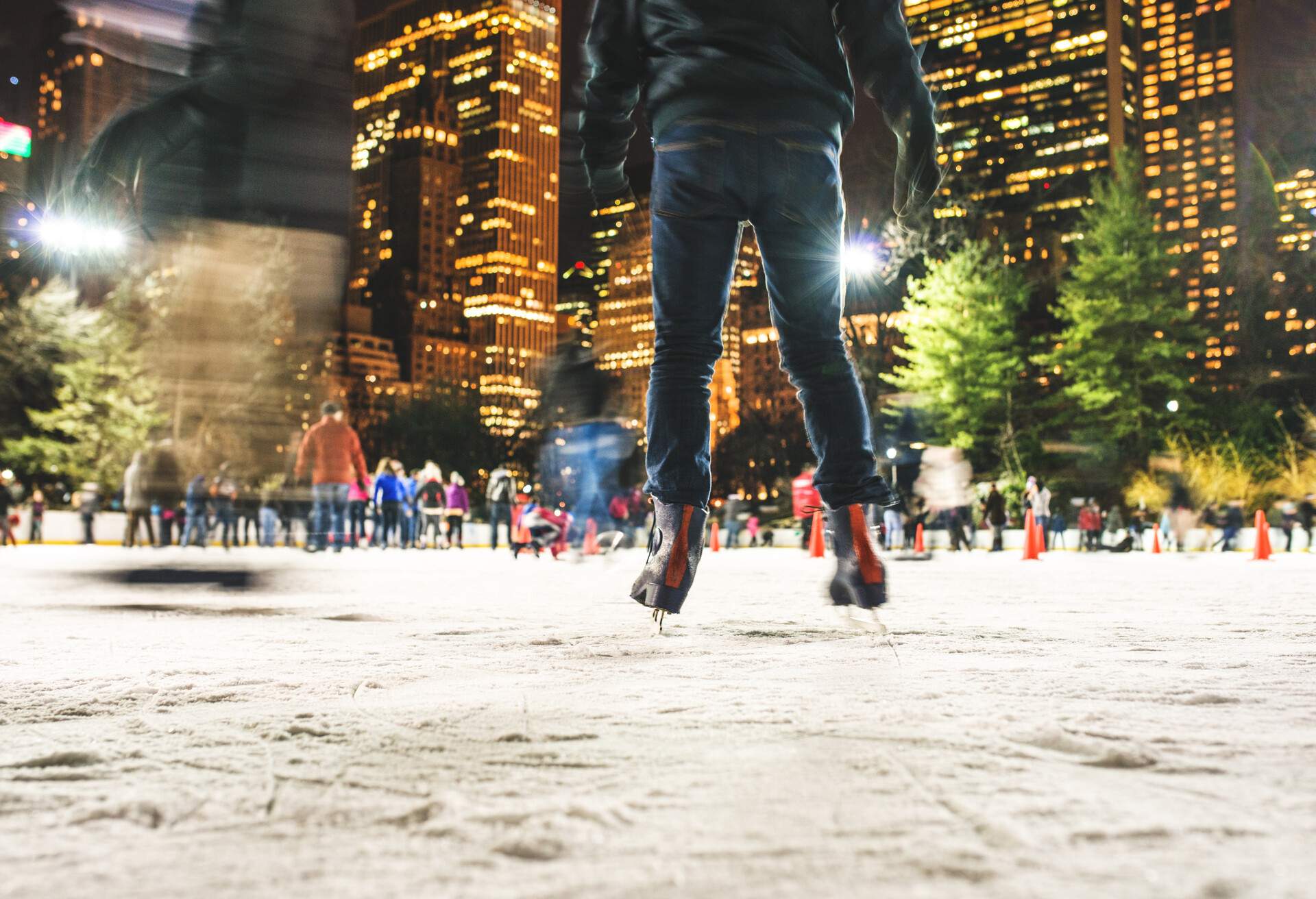 People skating on an ice rink surrounded by illuminated skyscrapers.
