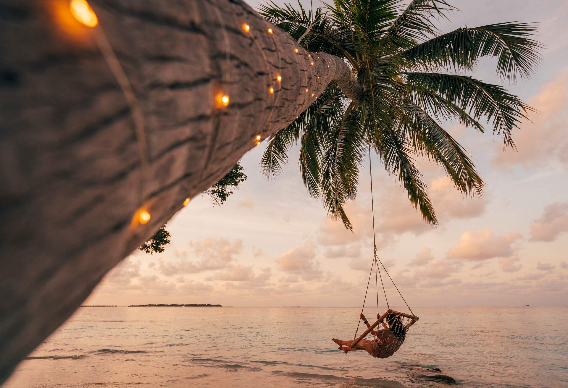A young adult woman finds tranquilly, gently swaying on a swing tied to a palm tree.