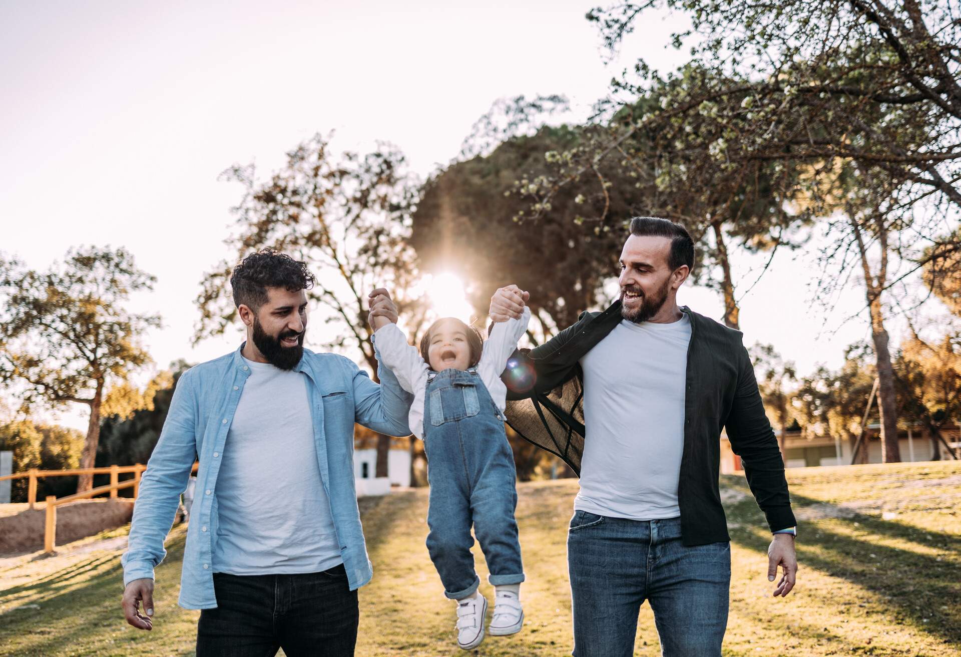 Male gay couple lift up their little girl who is laughing happily. Diverse modern family concept.