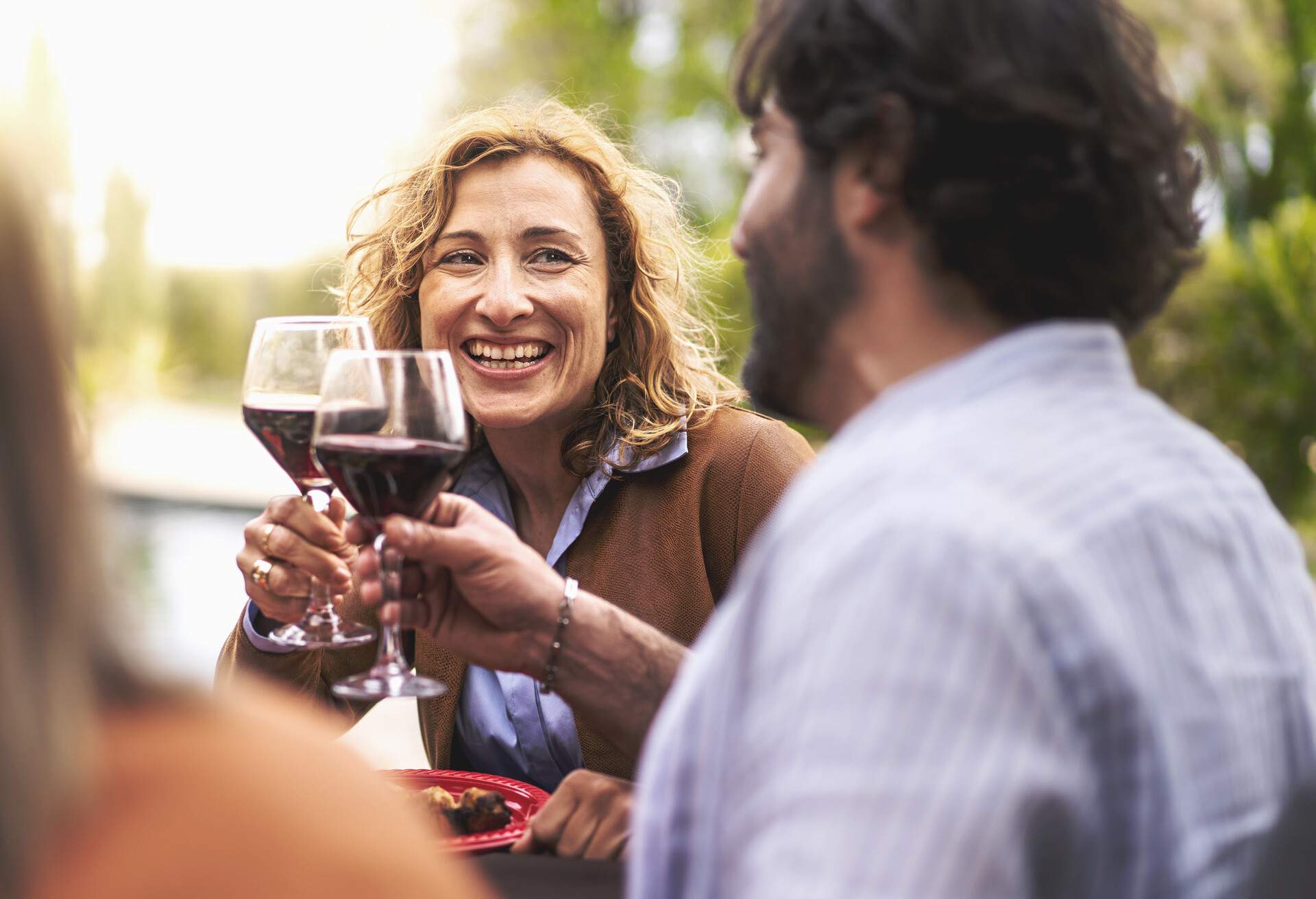 Happy couple of 40s people having fun toasting outdoors sitting at the barbecue table - lifestyle conviviality concept - forty-year-olds at the table in a carefree afternoon