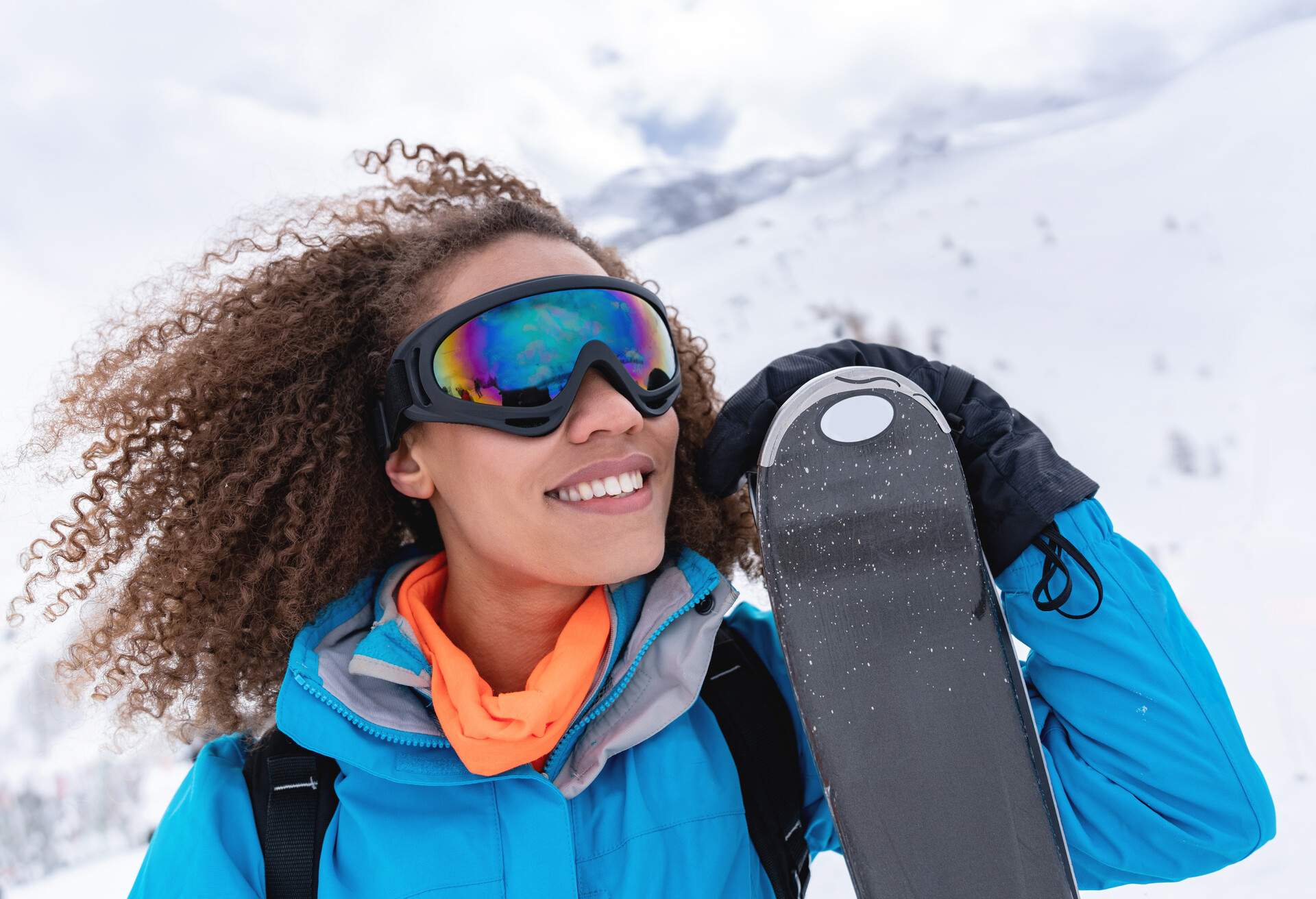 African American female skier looking very happy in the mountains enjoying the snow and holding her skies while wearing goggles and smiling